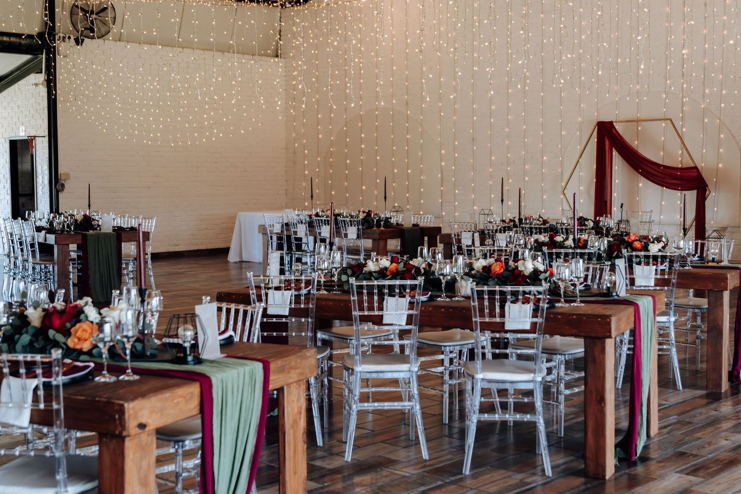 Elegant wedding reception venue with fairy lights, wooden tables, white chiavari chairs, and colorful floral centerpieces.