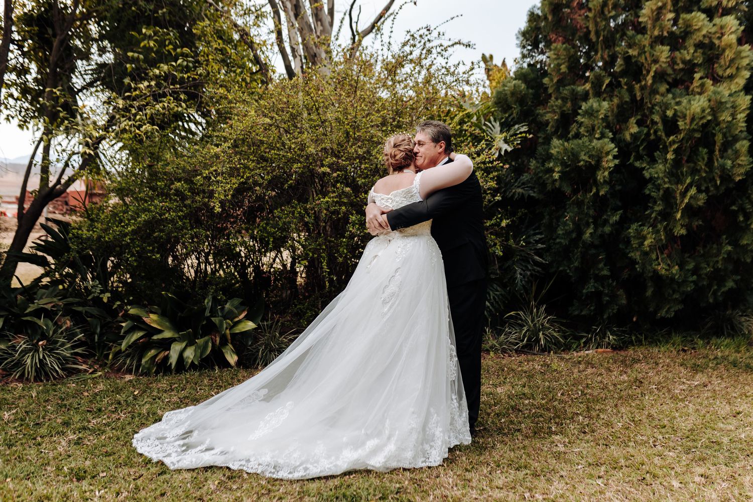 A romantic outdoor wedding moment captured in a garden setting with a flowing white gown against lush greenery.