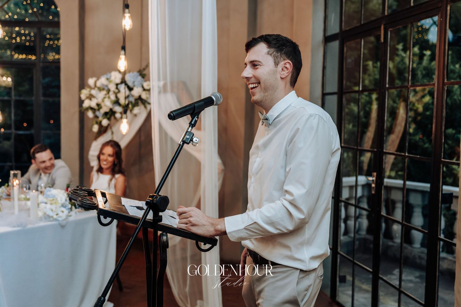 A speaker delivers a speech at an elegant outdoor reception with string lights.