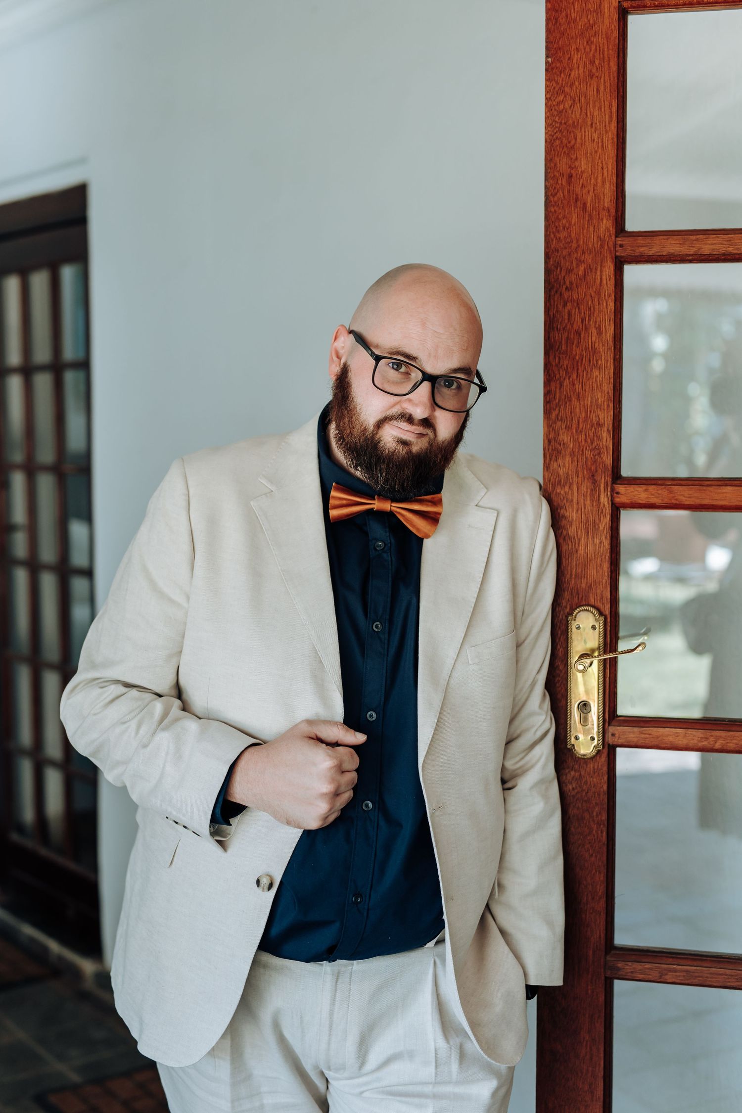 A person in a white blazer and black shirt poses in a sequence of four photos against a wooden door frame.