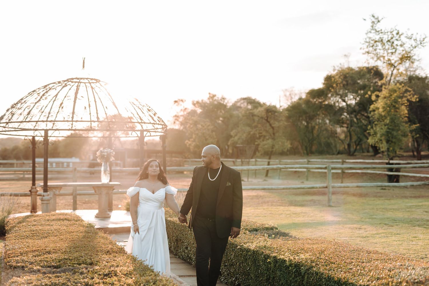 Newlyweds walk together under gazebo during golden hour wedding photoshoot.