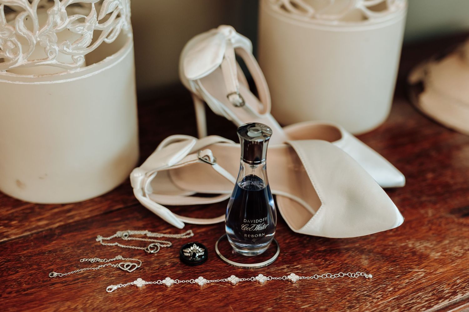Elegant wedding details with decorative vessels and small perfume bottle on dark wood table.