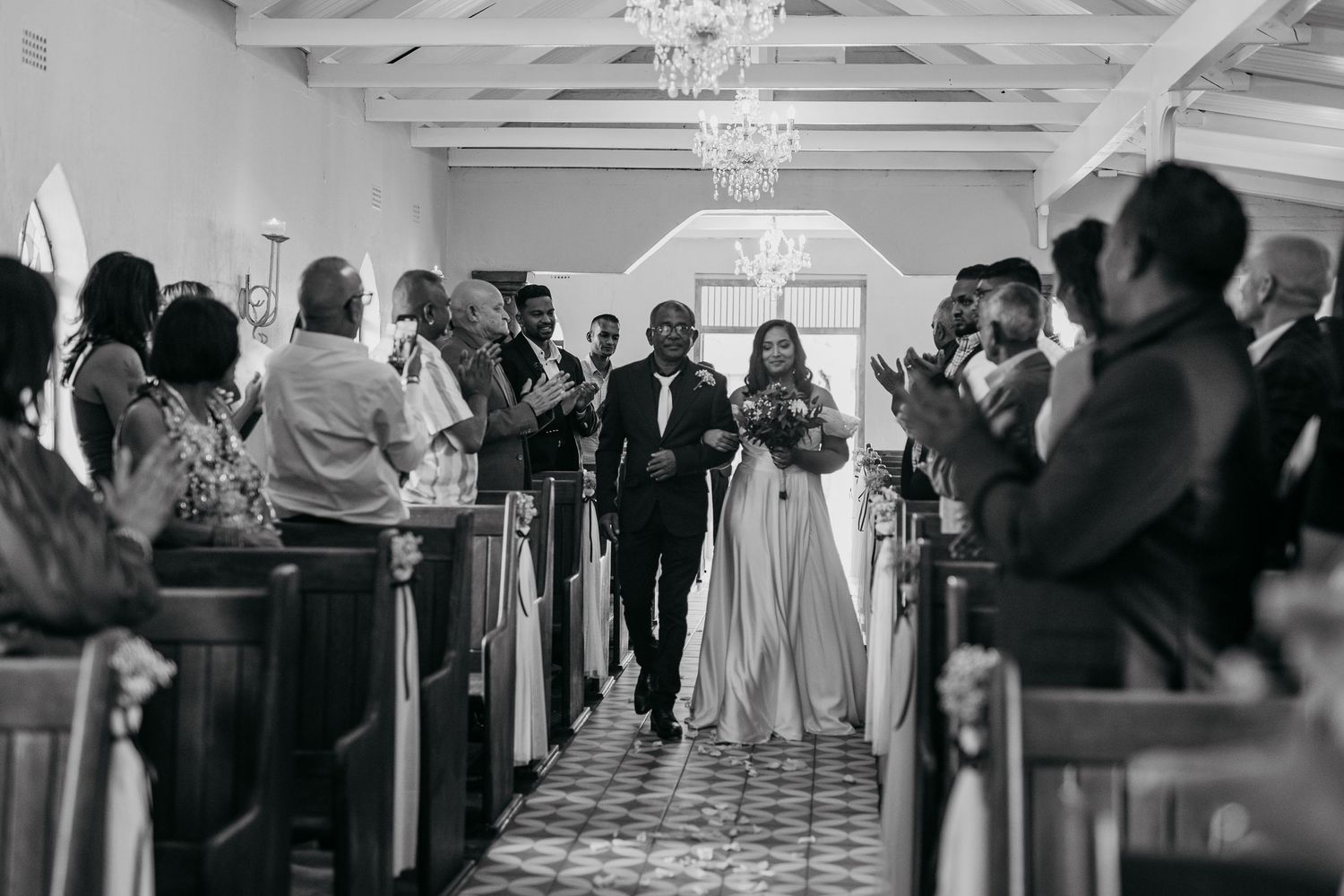 Wedding guests standing and applauding as the newlyweds walk down the aisle.