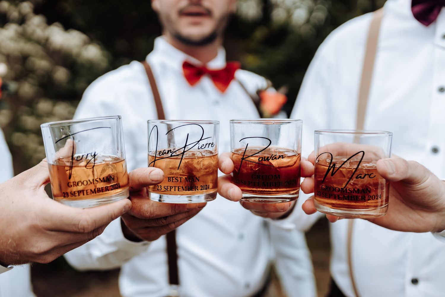 Groomsmen toast with personalized whiskey glasses at outdoor celebration.