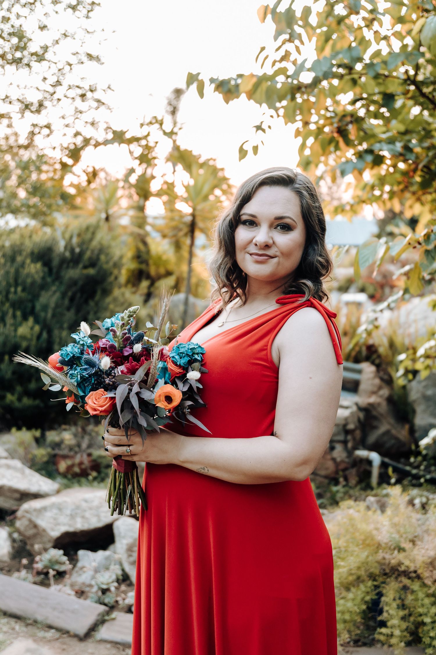 Person in red dress holding vibrant floral bouquet in garden setting during golden hour.