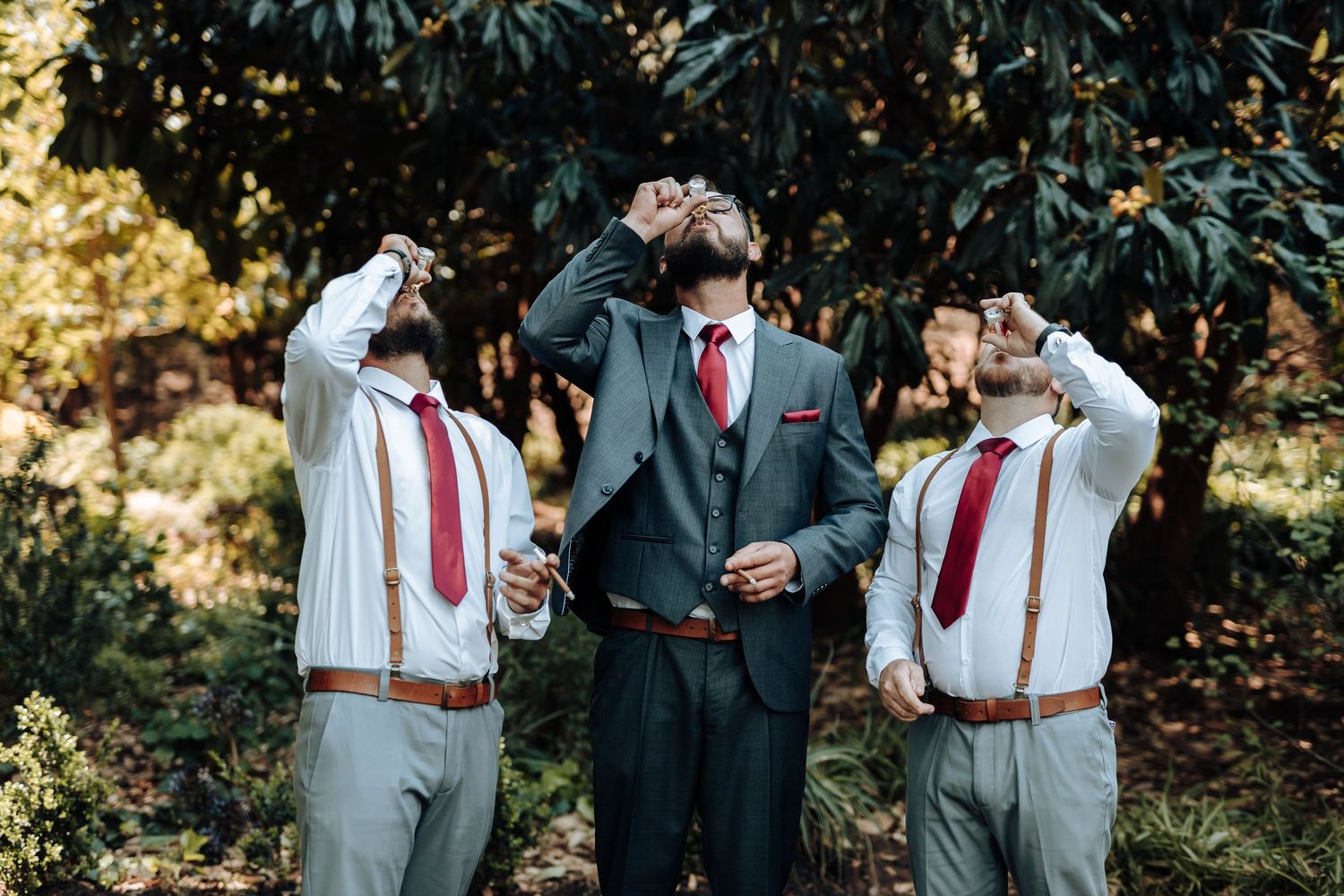 Groomsmen in coordinated attire taking synchronized drinks in an outdoor setting.