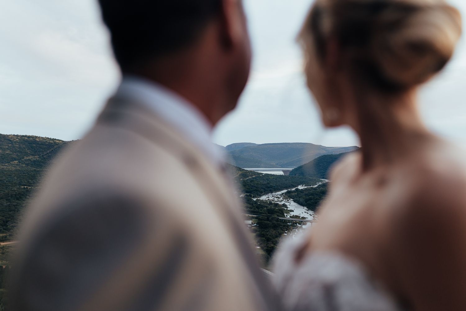 Bride and groom share an intimate moment overlooking mountain valleys in soft focus.