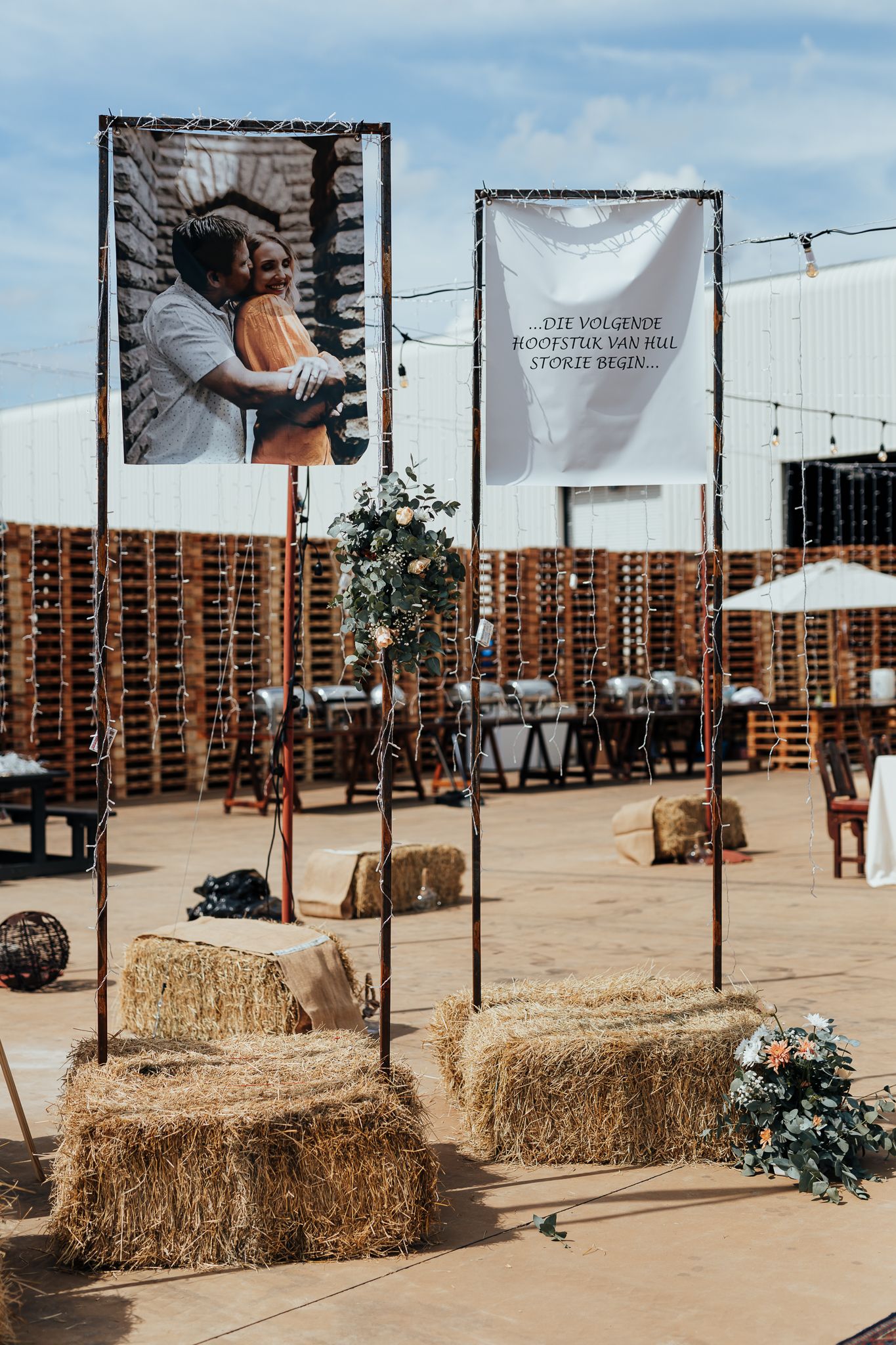 Wedding venue decorated with large banners and hay bales in an industrial outdoor setting.