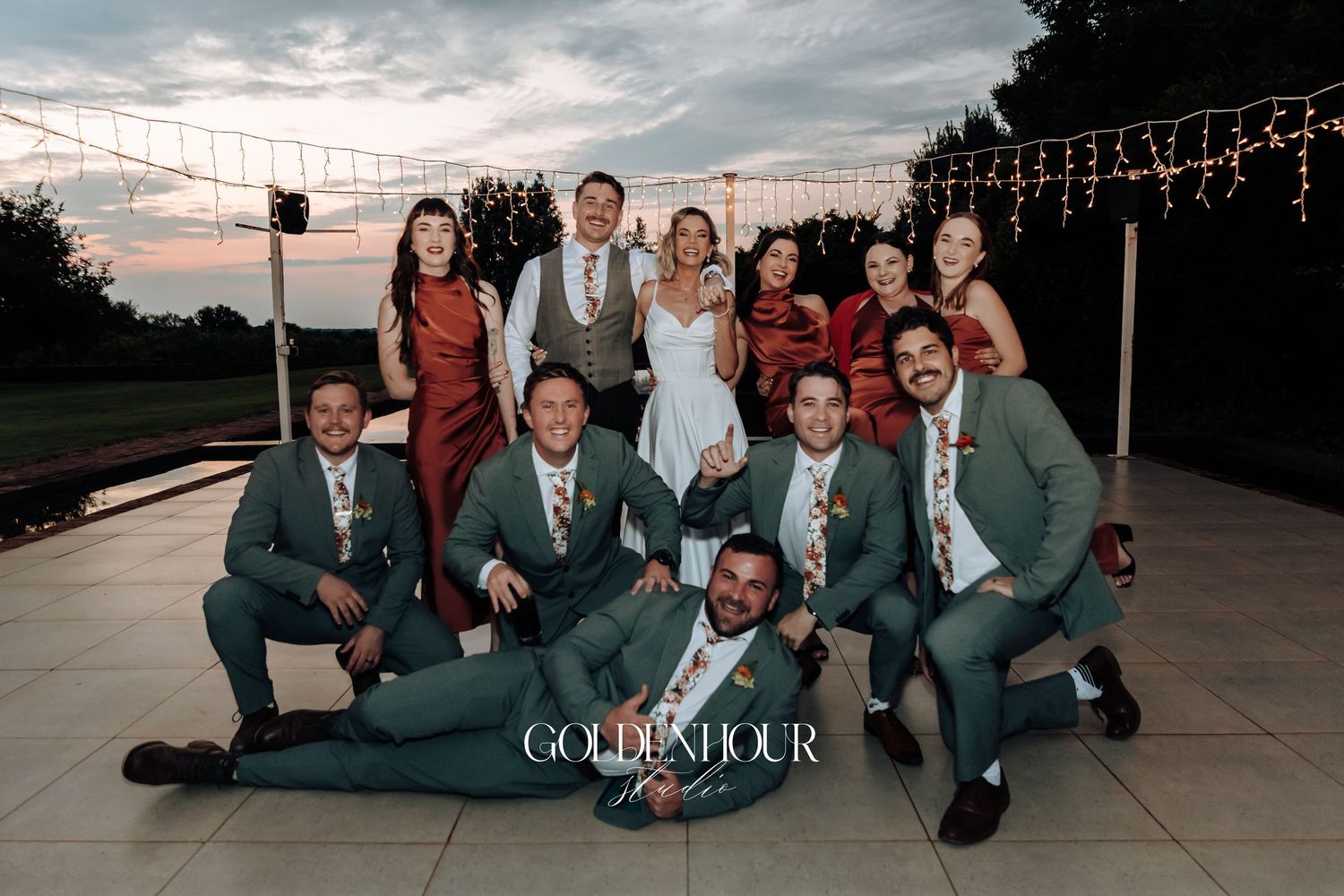 Wedding party in gray suits poses casually on the ground at dusk.