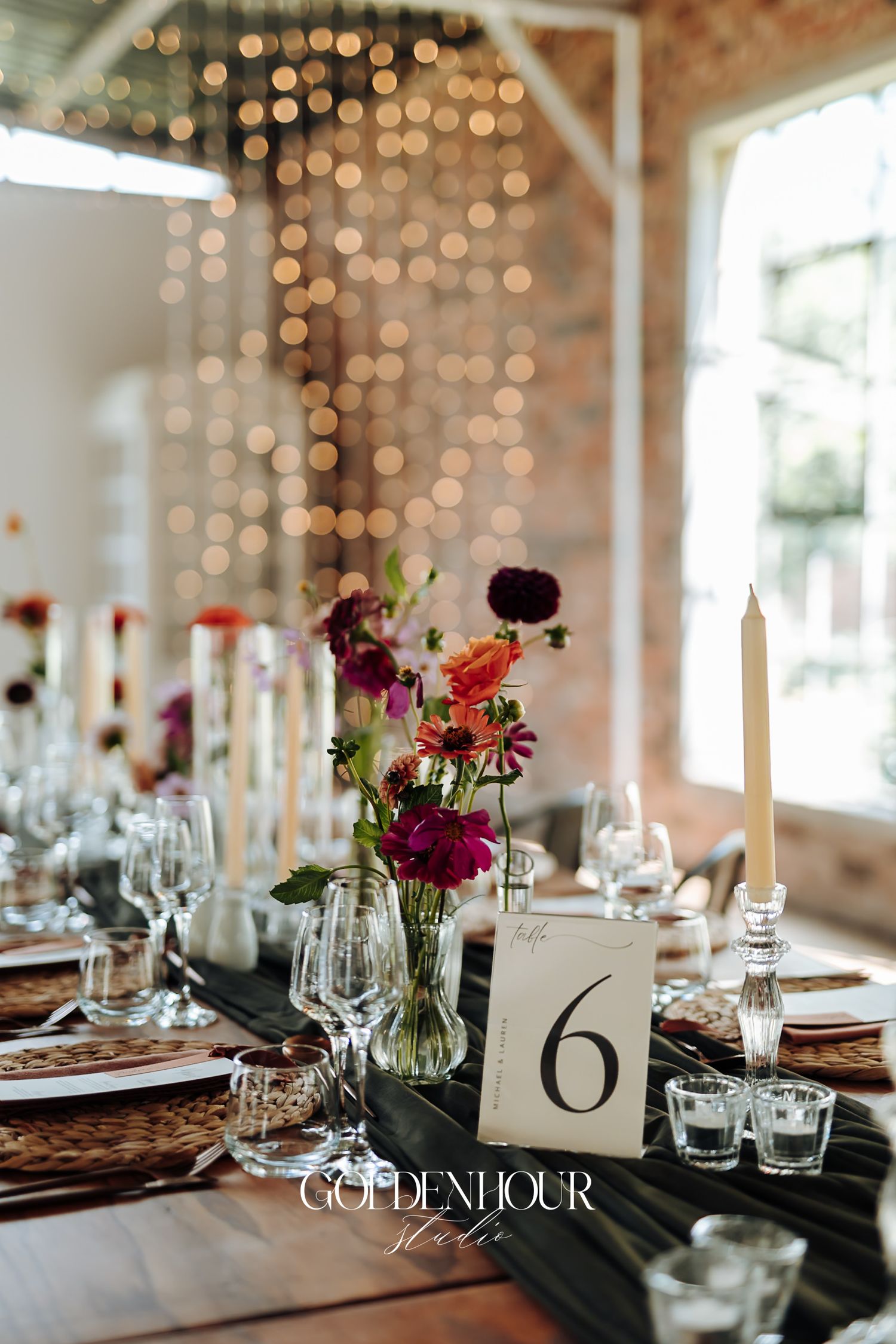 Romantic wedding reception table with colorful florals, taper candles, table number six, and bokeh string lights.