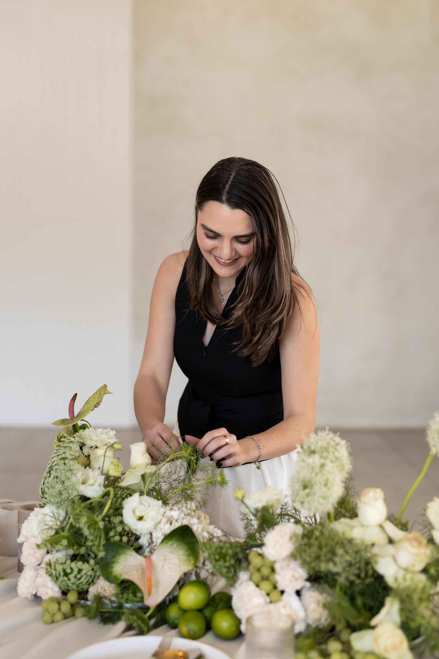 Professional floral designer arranging white flowers and greenery on a long table with green apples.