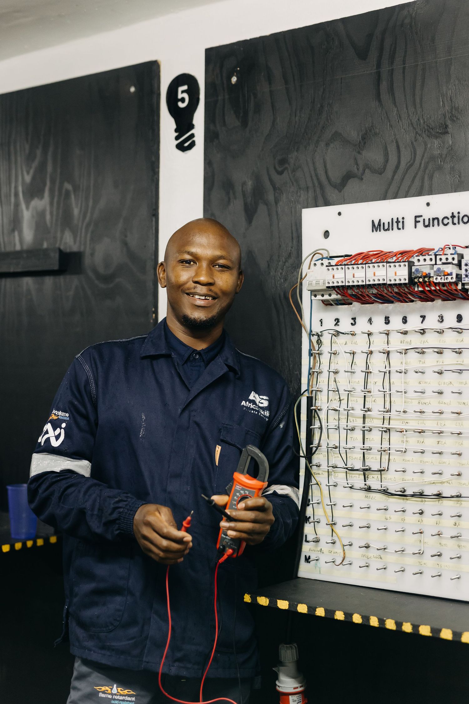 Electronics technician in navy uniform tests equipment with multimeter against calibration board in maintenance facility.