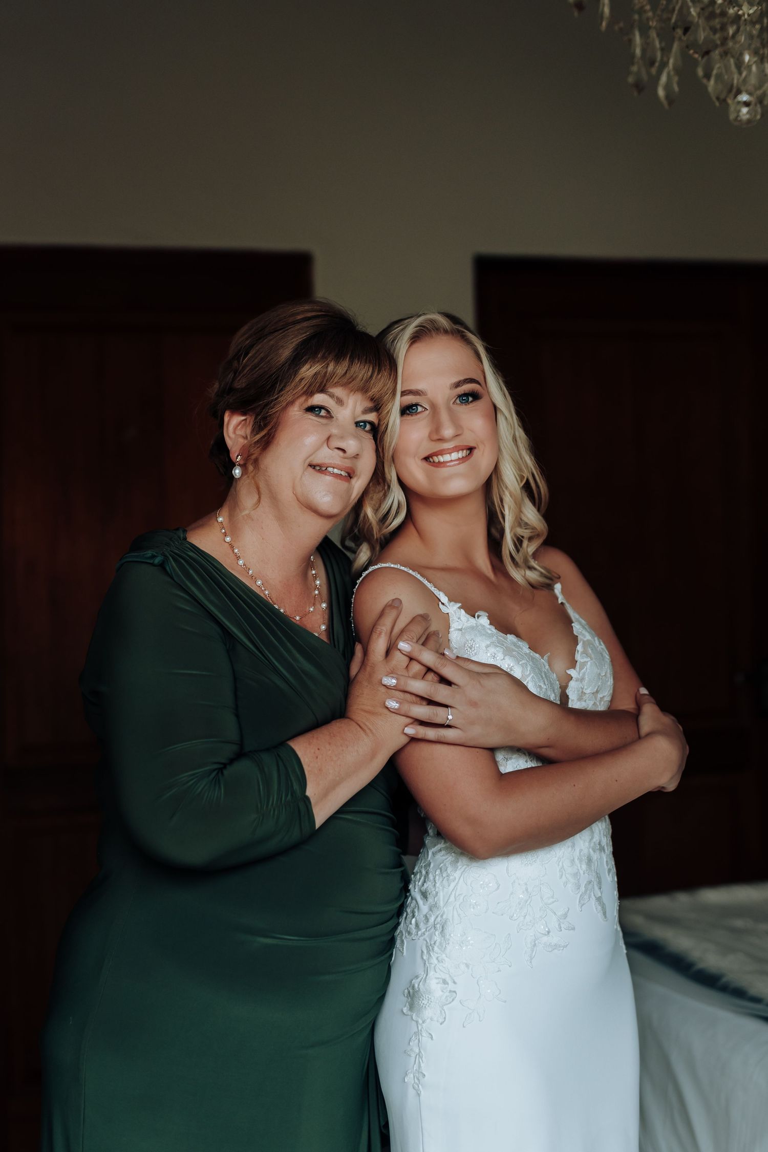 Two women pose together at a wedding, one wearing an emerald green dress and one in a white lace bridal gown.
