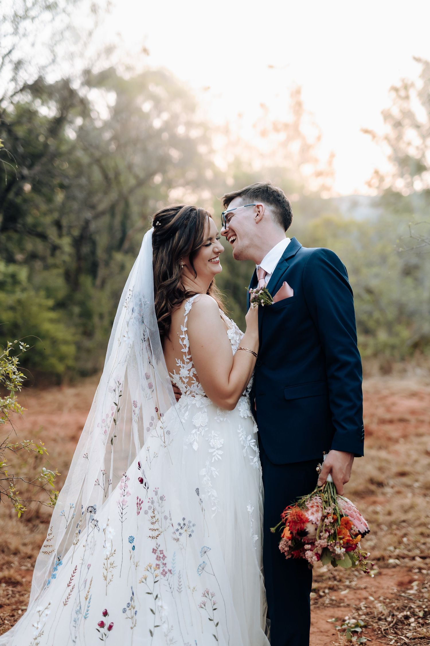 A couple shares romantic moments in their wedding attire surrounded by autumn foliage and soft sunlight.
