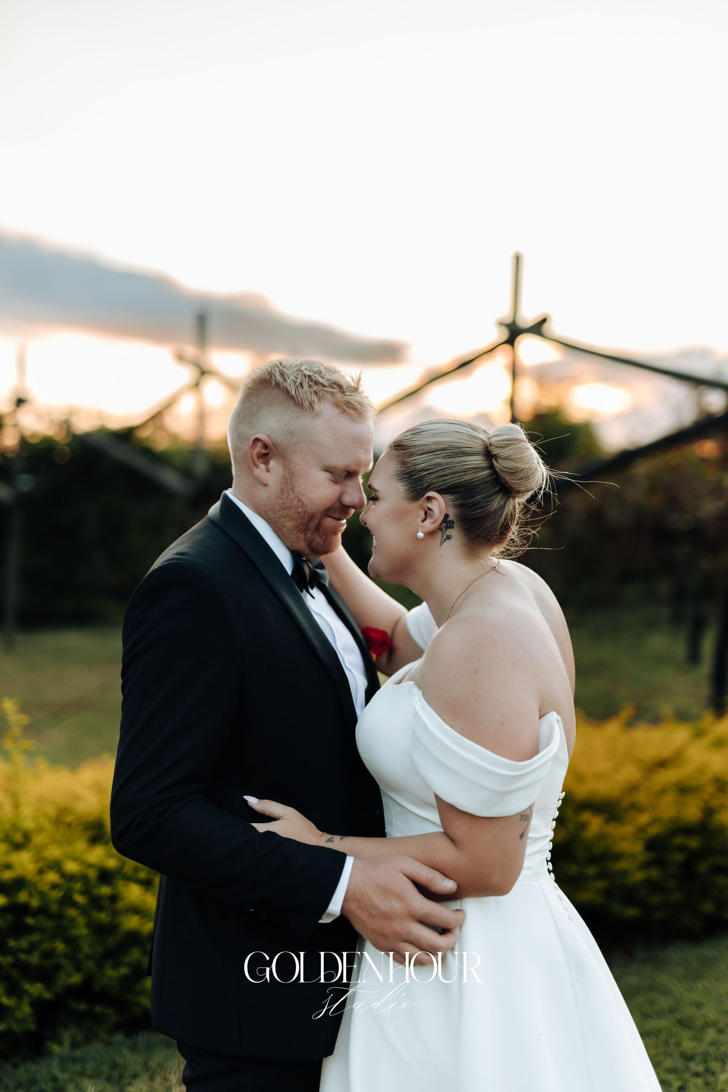 Romantic wedding couple embraces outdoors during golden hour sunset in a garden setting.