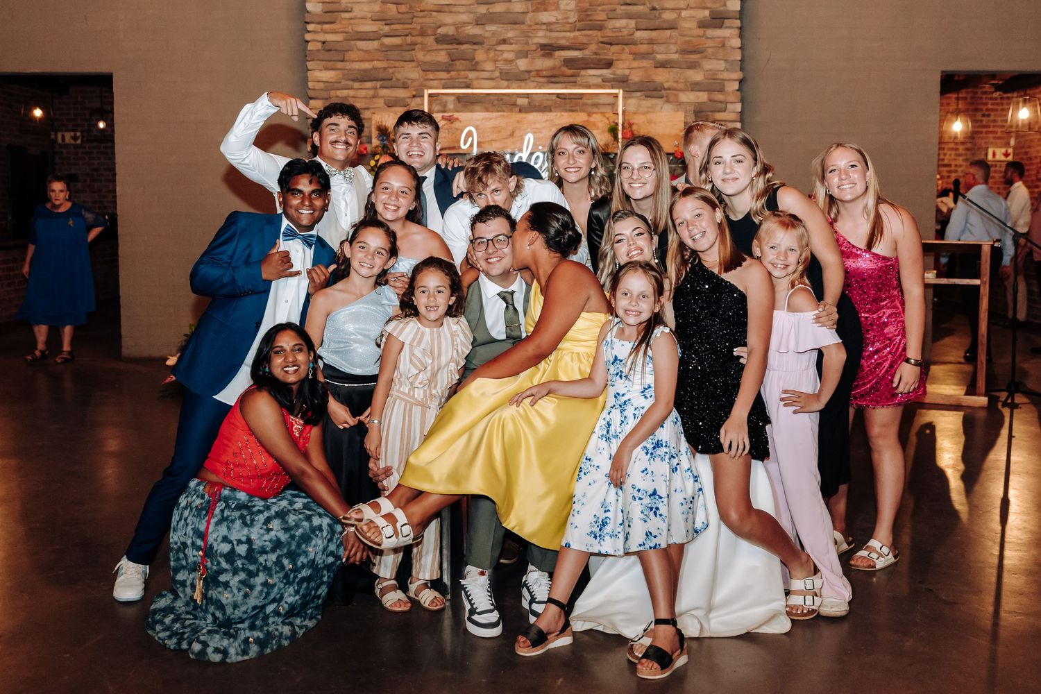 Large group of wedding guests posing together on dance floor at reception venue.