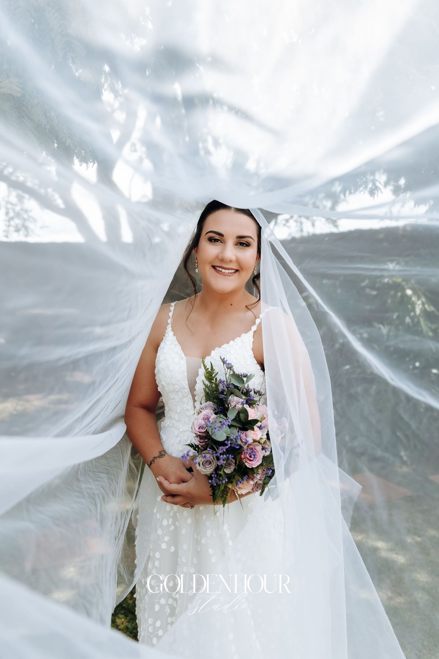 Dramatic bridal portrait with flowing veil and mixed flower bouquet against dreamy background.