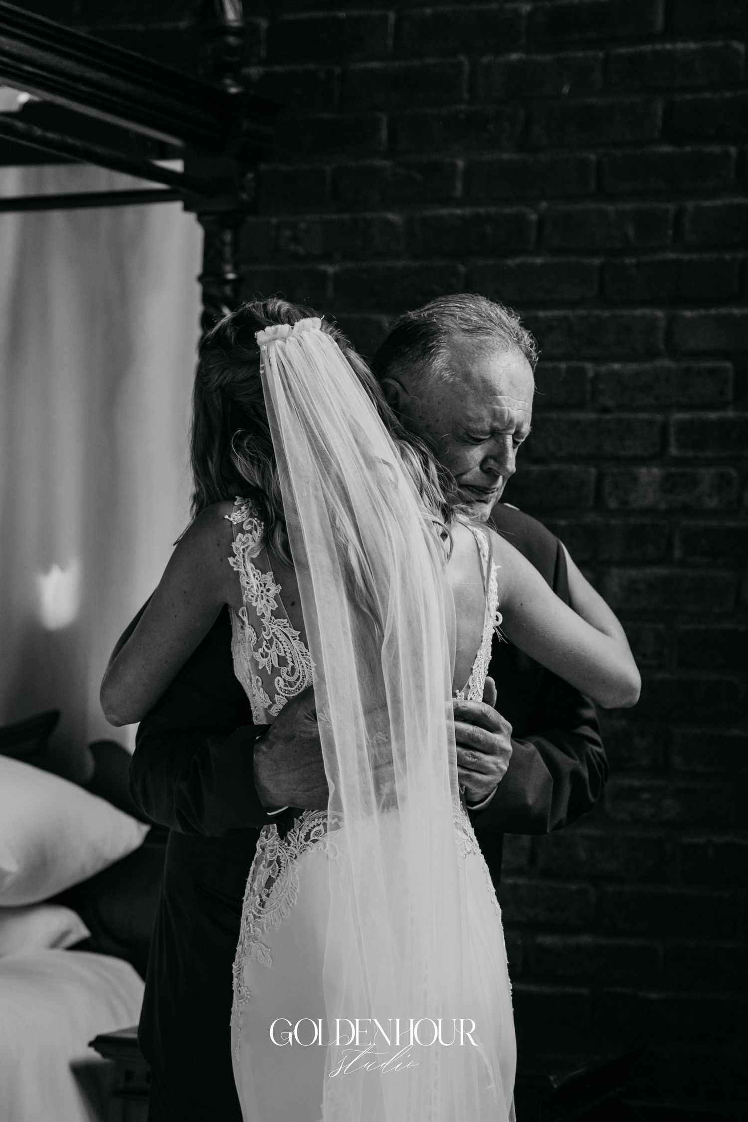 Emotional black and white wedding moment captured against brick wall backdrop.