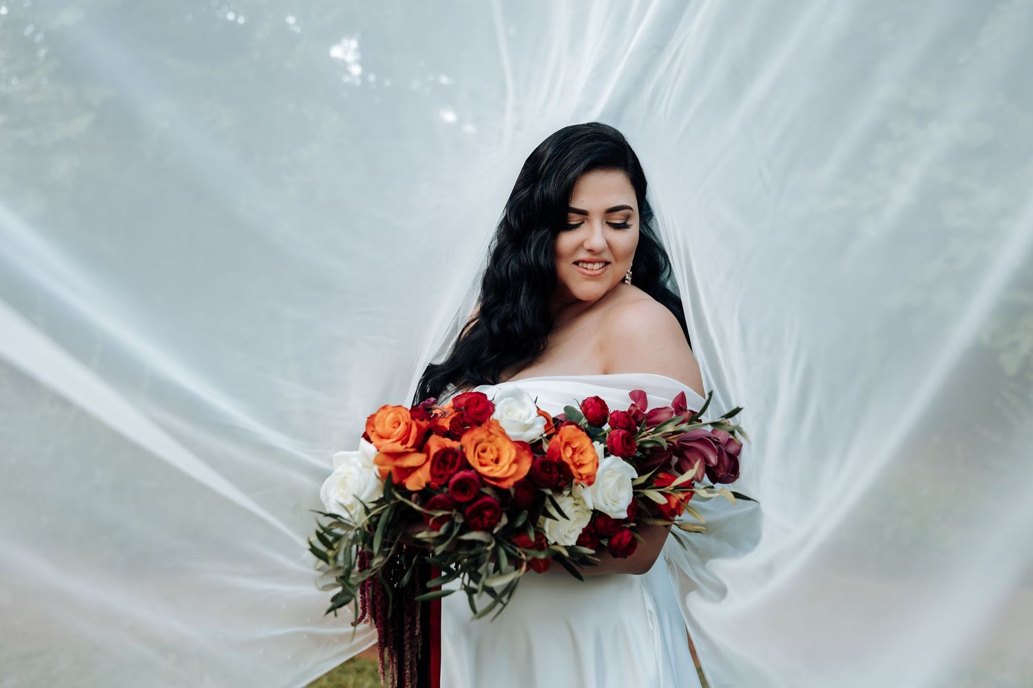 Elegant bridal portrait with vibrant red and burgundy bouquet against white backdrop.