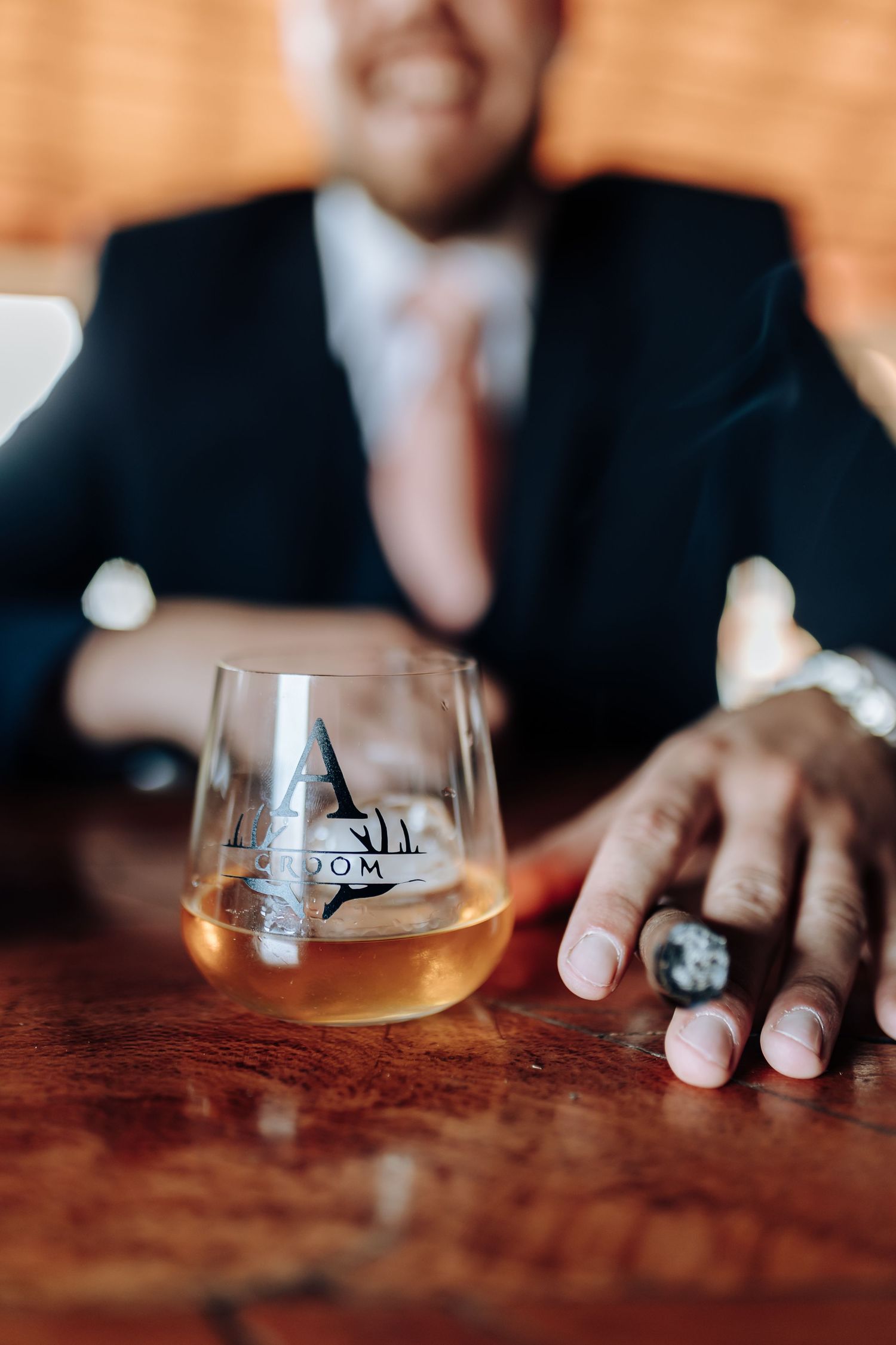 Hands resting on a wooden table next to glasses of beer or whiskey create an intimate bar atmosphere.