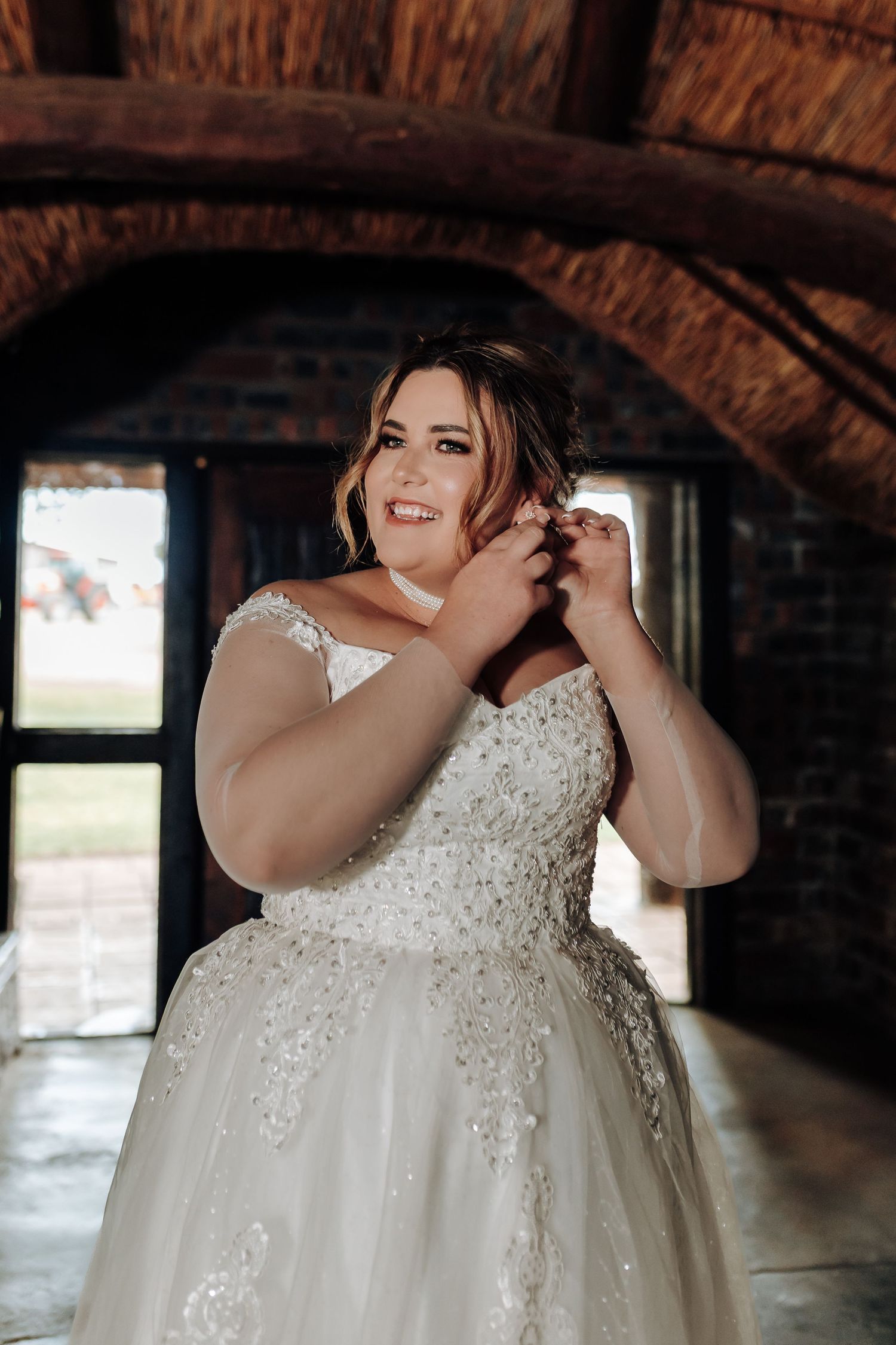Wedding preparations in a rustic brick venue showing close-up details of a bride's white beaded lace gown.