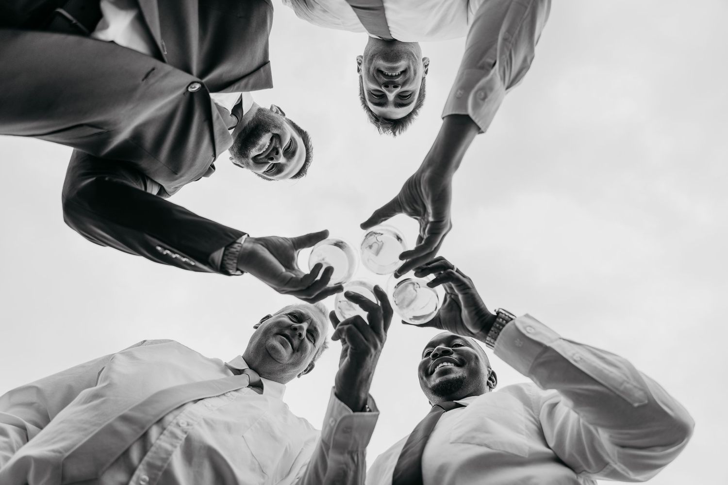 Black and white low angle view of a group in formal attire forming a circle while looking down at the camera.