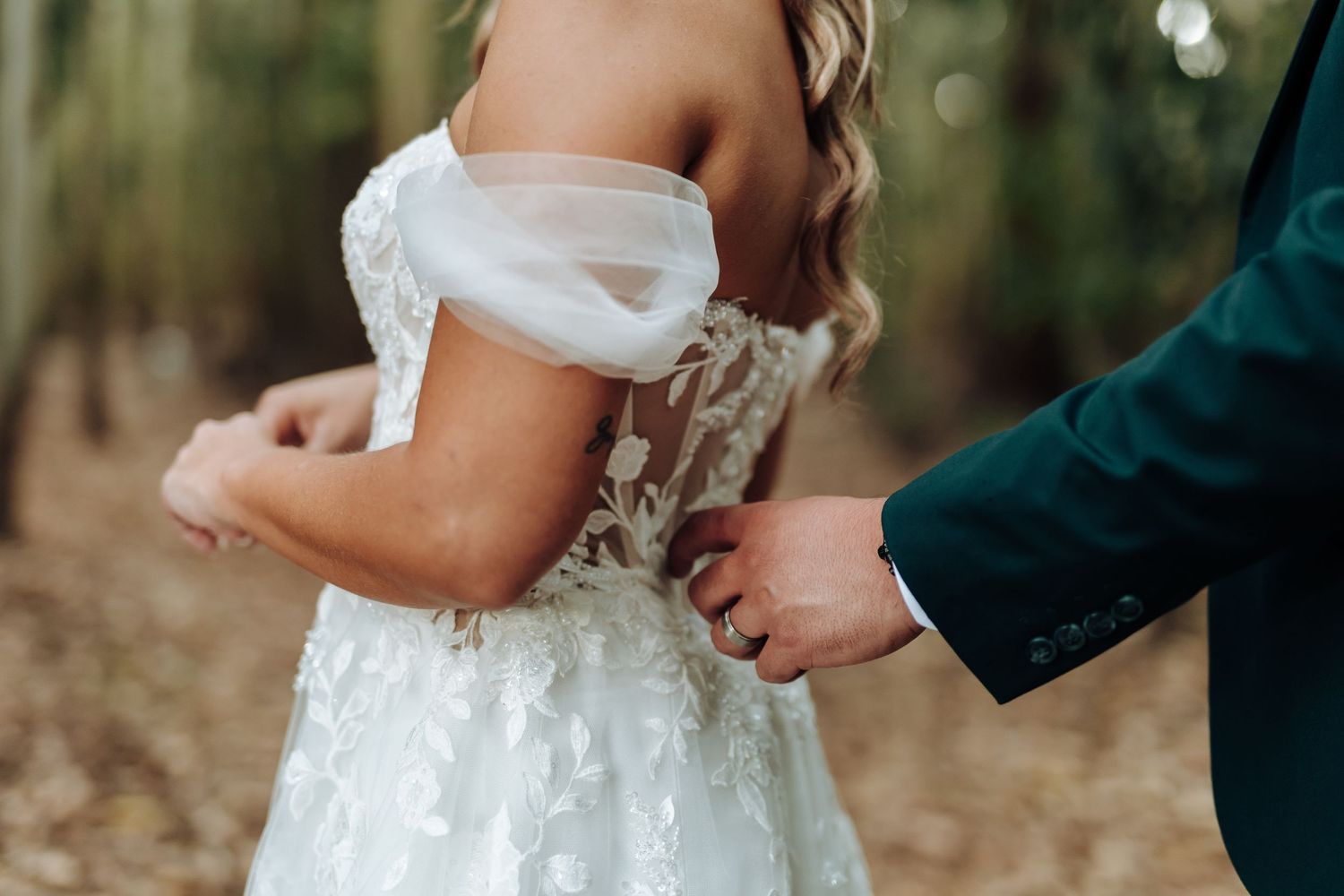 Close-up of hands adjusting delicate white lace wedding dress details in a forest setting.
