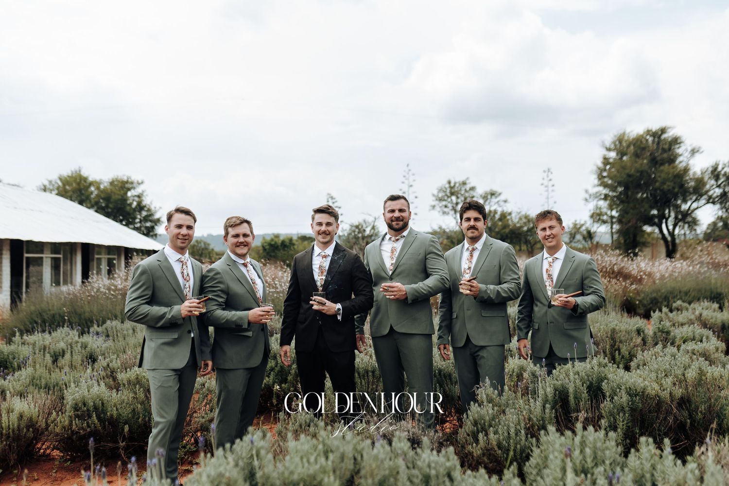 Wedding party in sage green attire posing together in front of desert brush landscape.