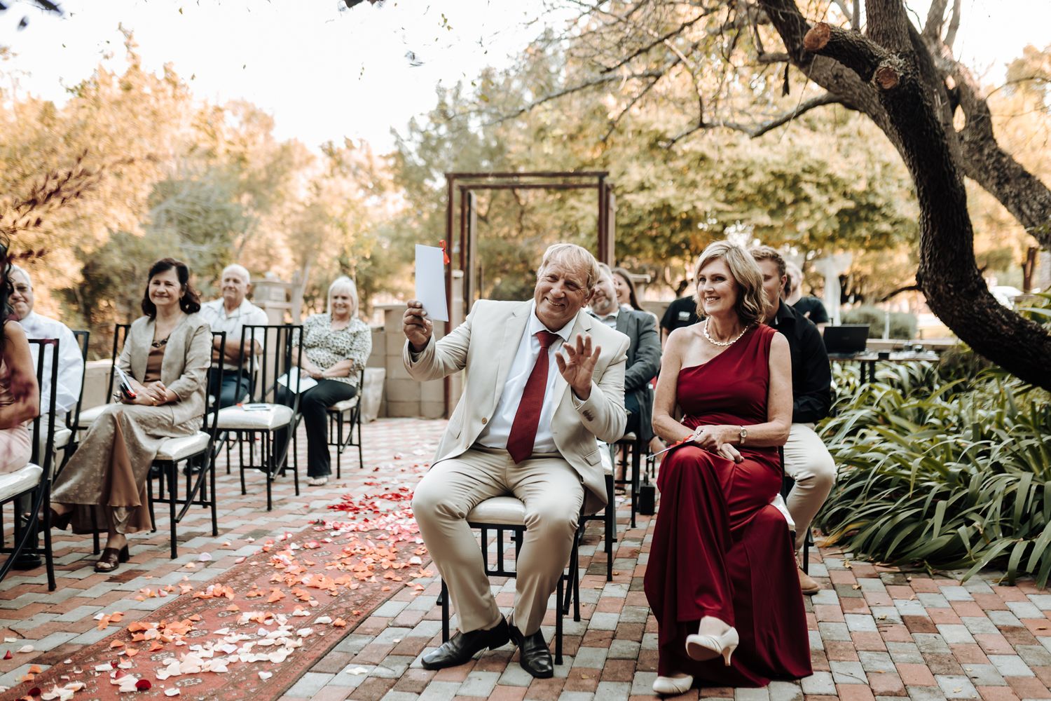 Outdoor wedding ceremony seating with red rose petals scattered on brick pathway.