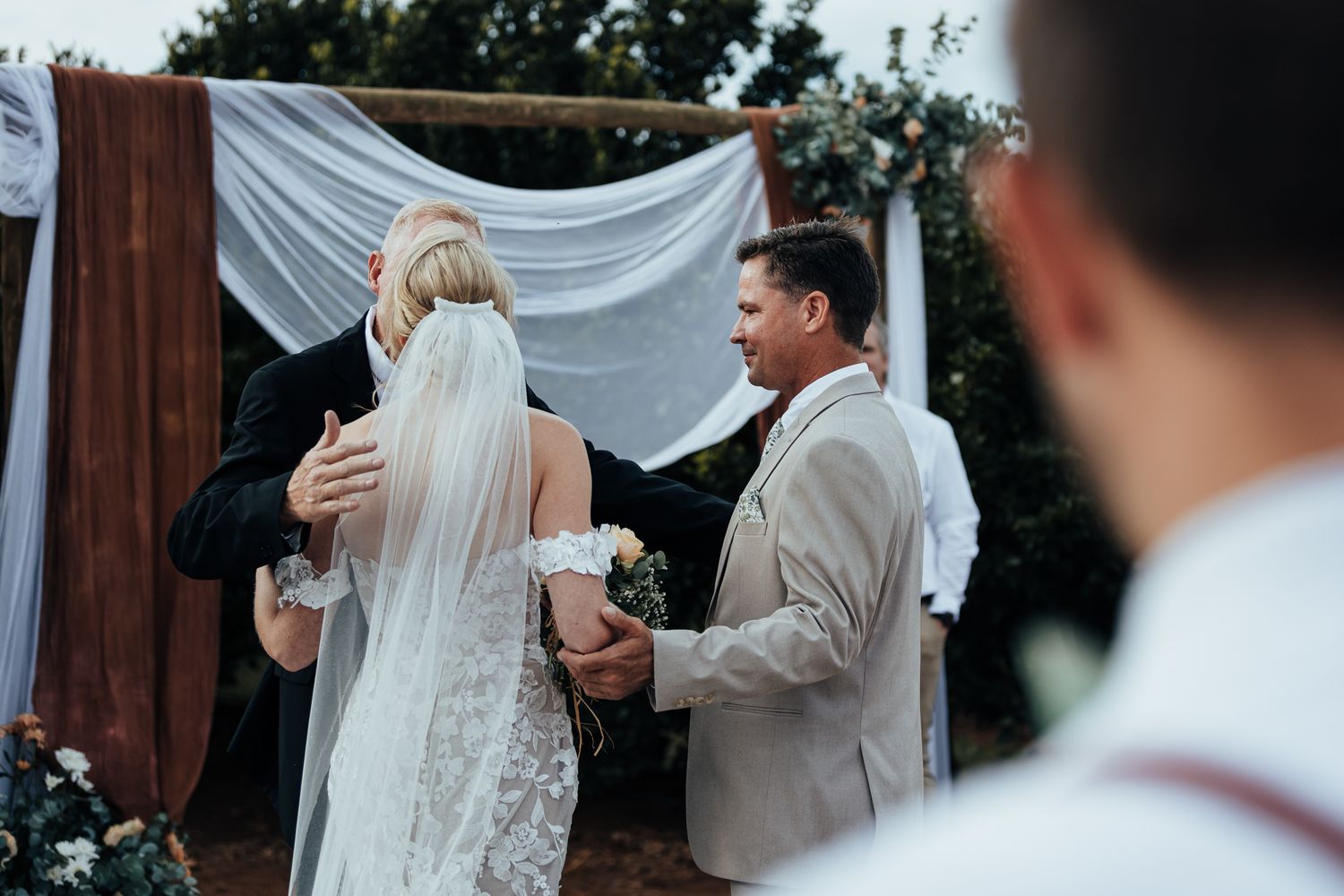 Wedding ceremony moment with couple and officiant at wooden arch with white fabric.