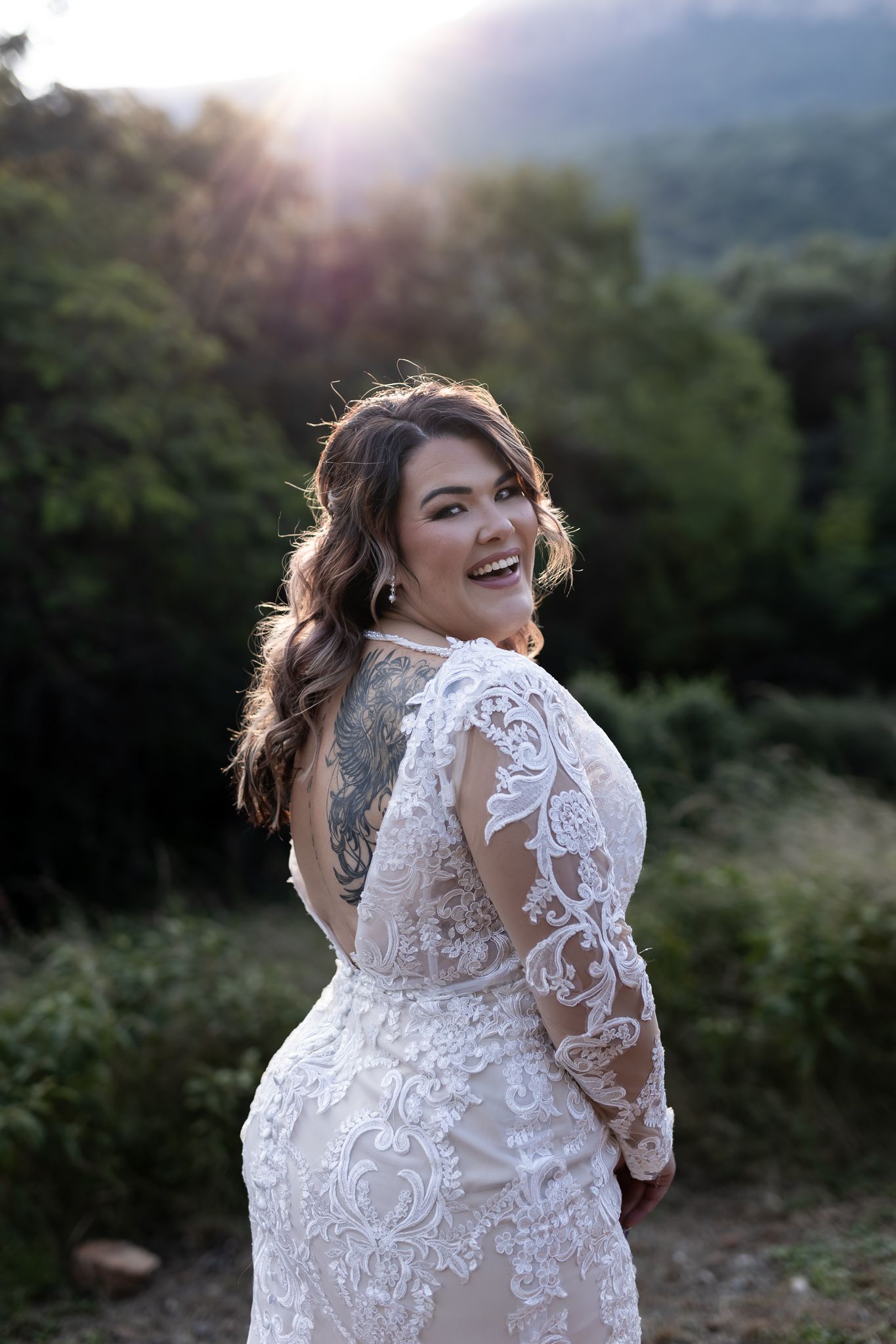 Radiant bride in backless lace gown smiles during golden hour photography.