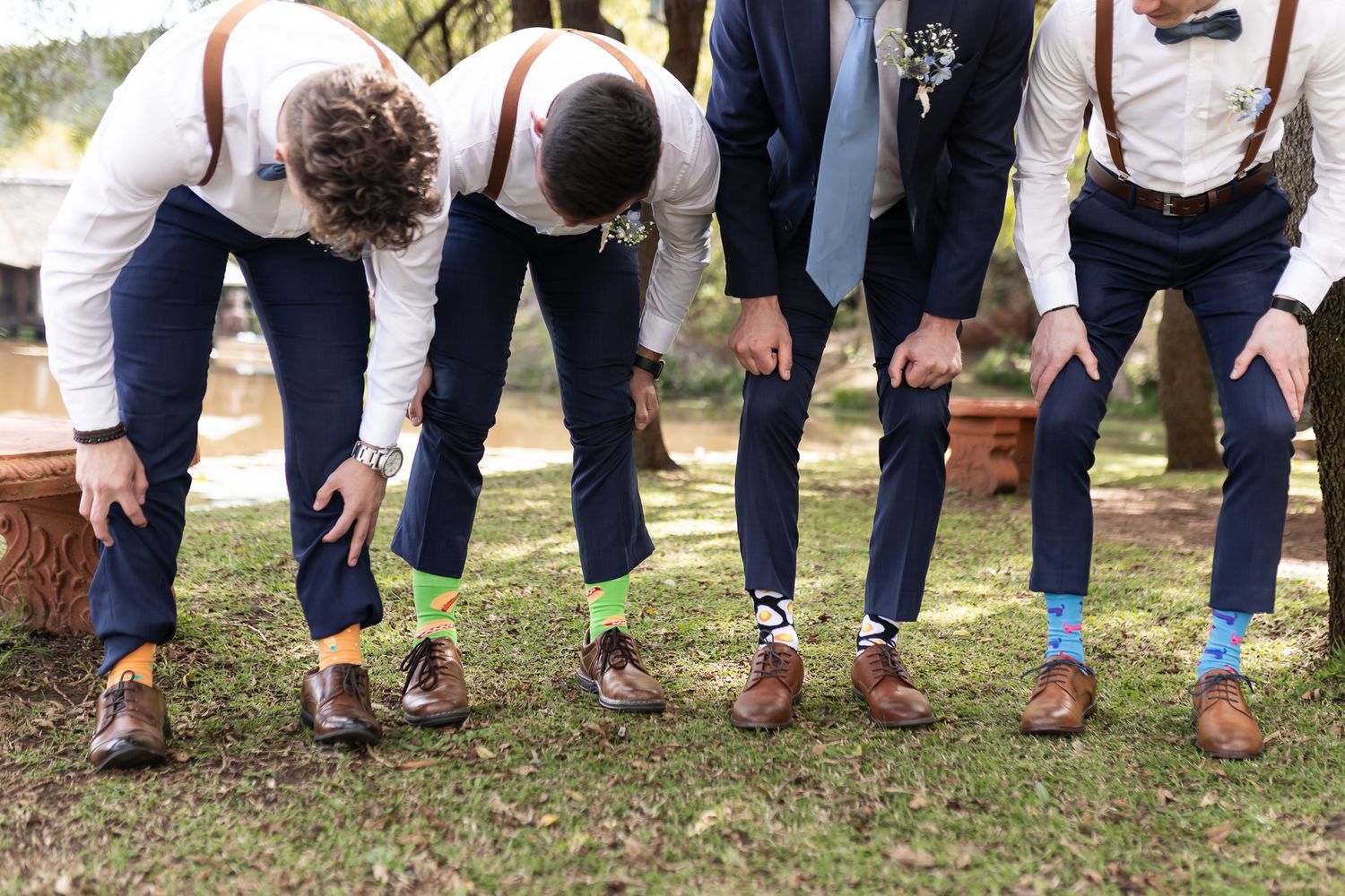 Groomsmen showing off colorful socks in synchronized pose outdoors.