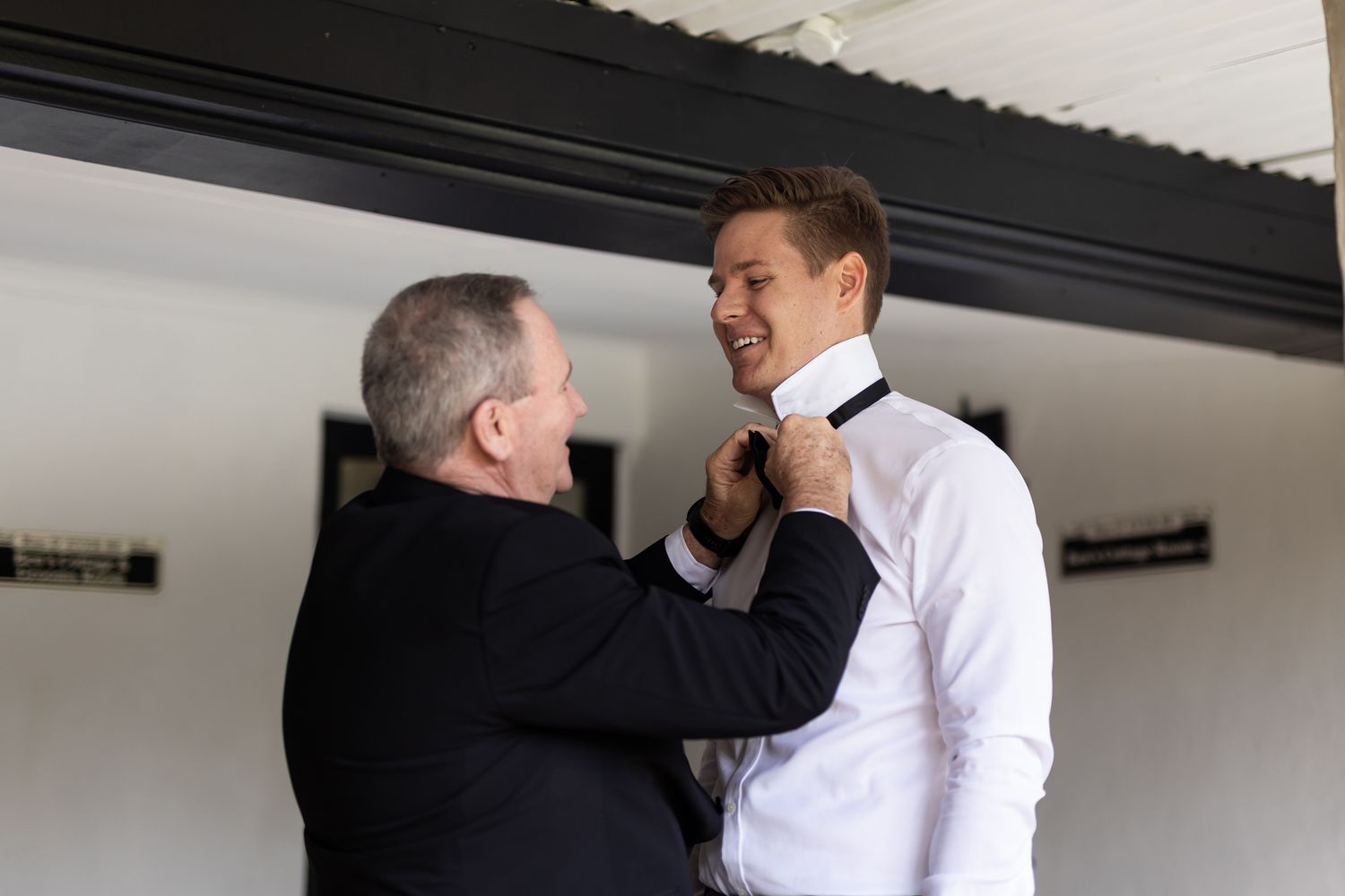 Two people sharing a formal dressing moment in a white room.