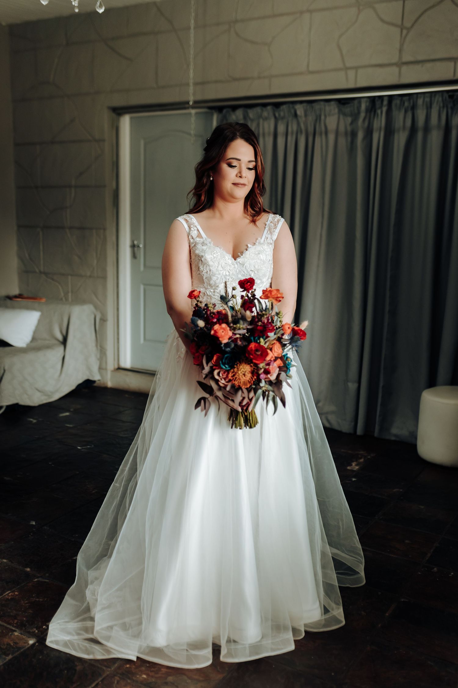 Full-length view of bride in v-neck wedding gown holding vibrant red and pink bouquet.