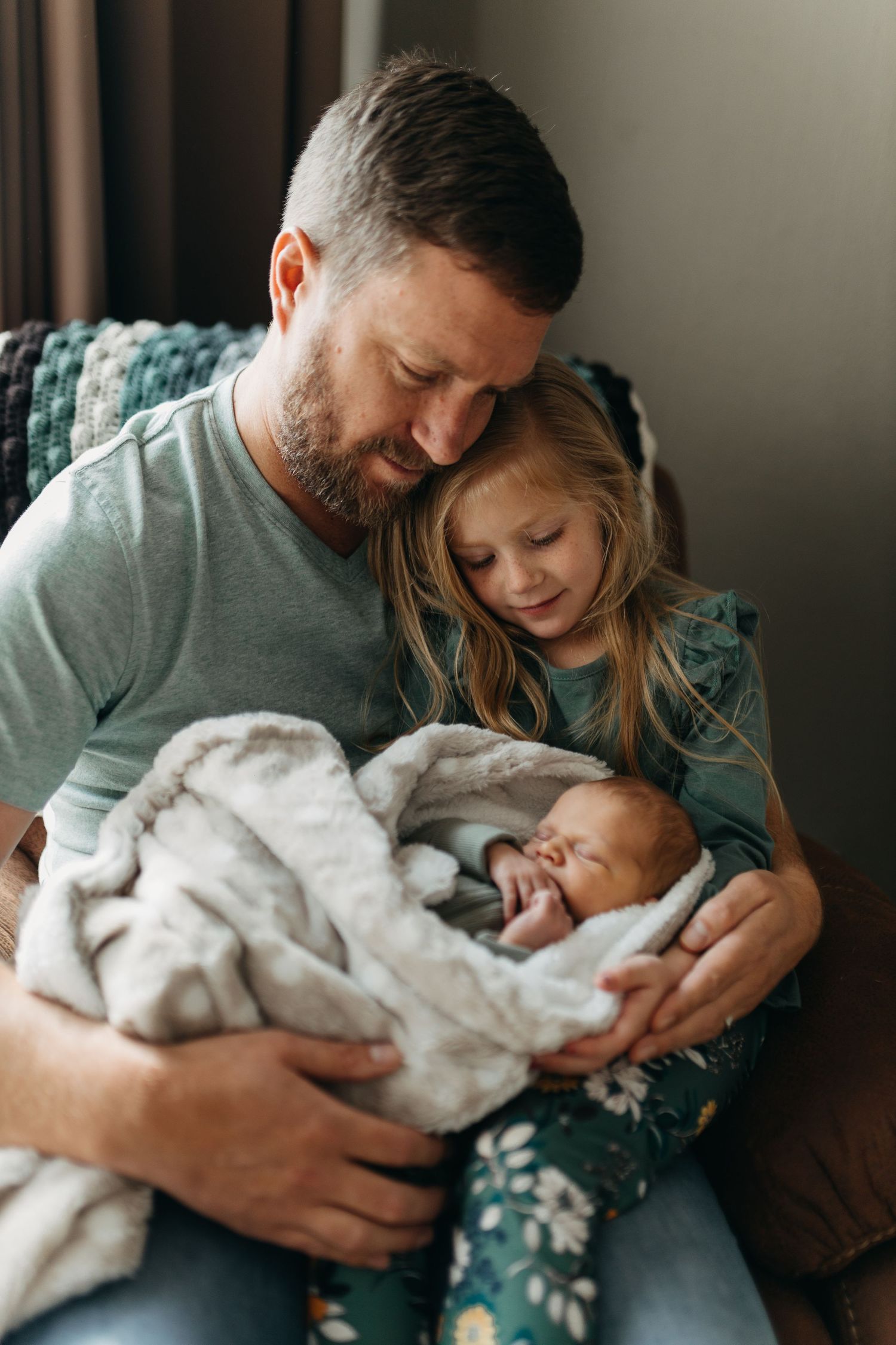 Loving parents cuddle with their newborn baby on a couch in a tender family moment at home.
