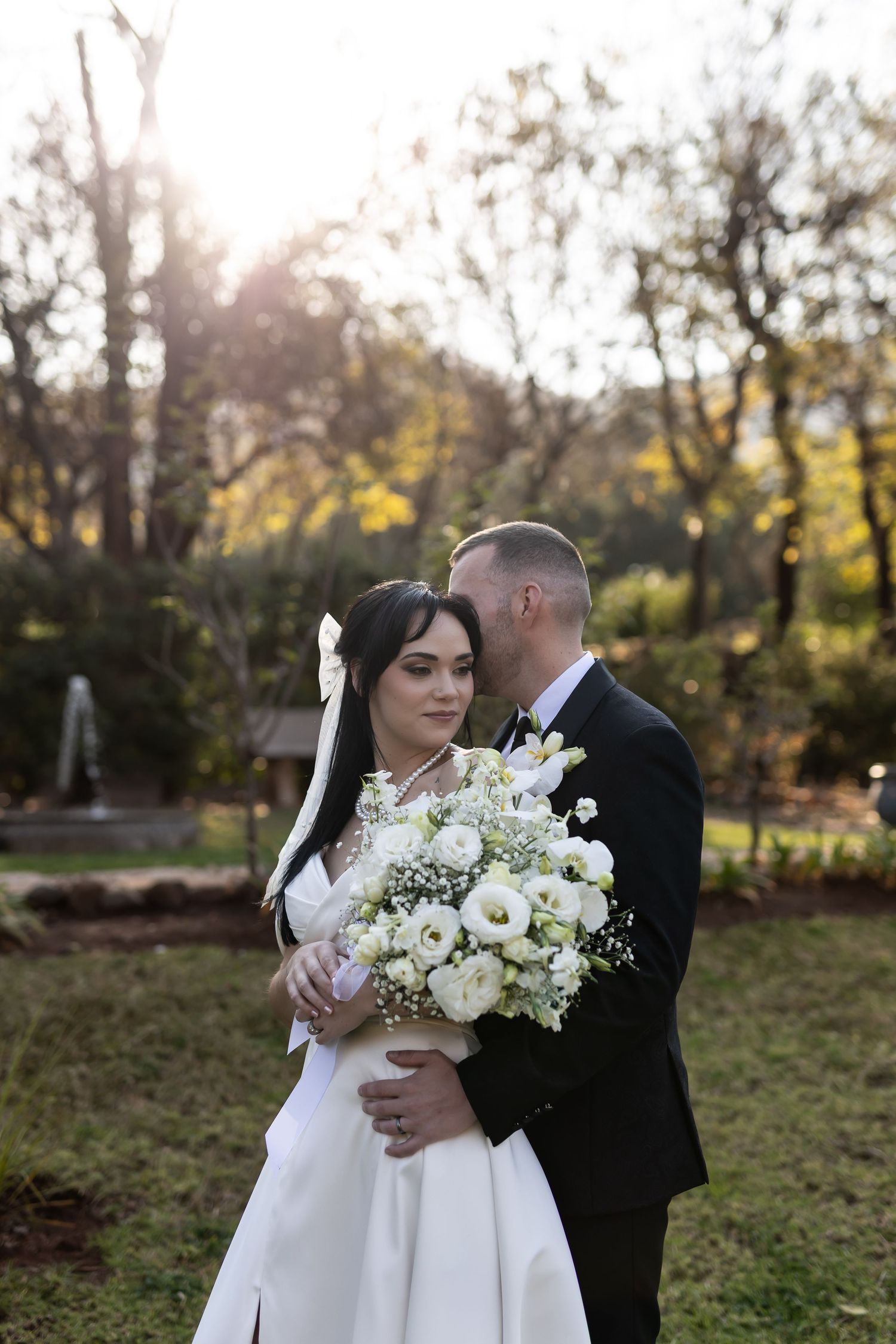 Newlywed couple shares intimate moment outdoors with bride holding elegant white floral bouquet in autumn garden setting.