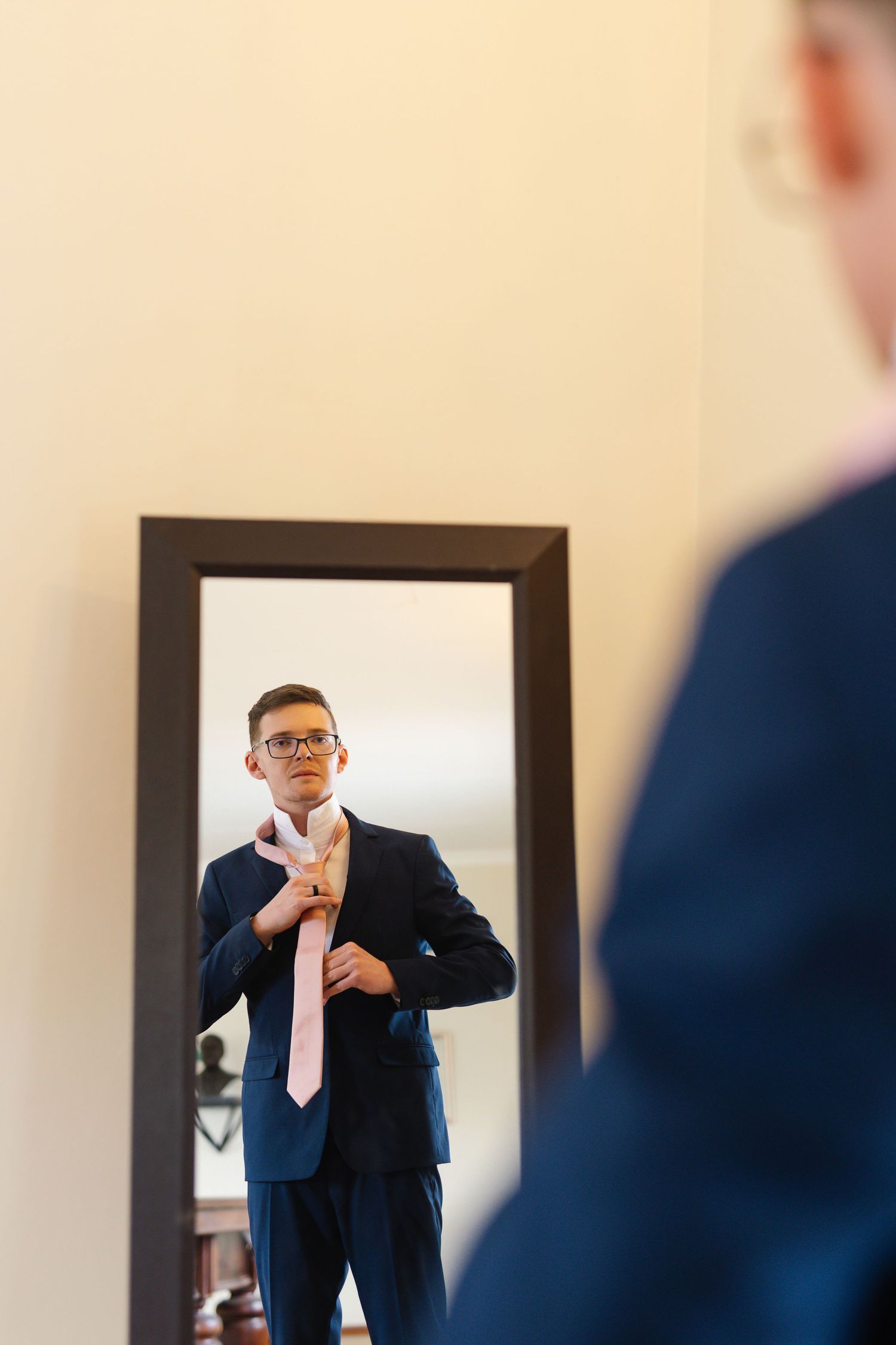 Professional in a navy suit and glasses gestures while giving a business presentation in an office setting.