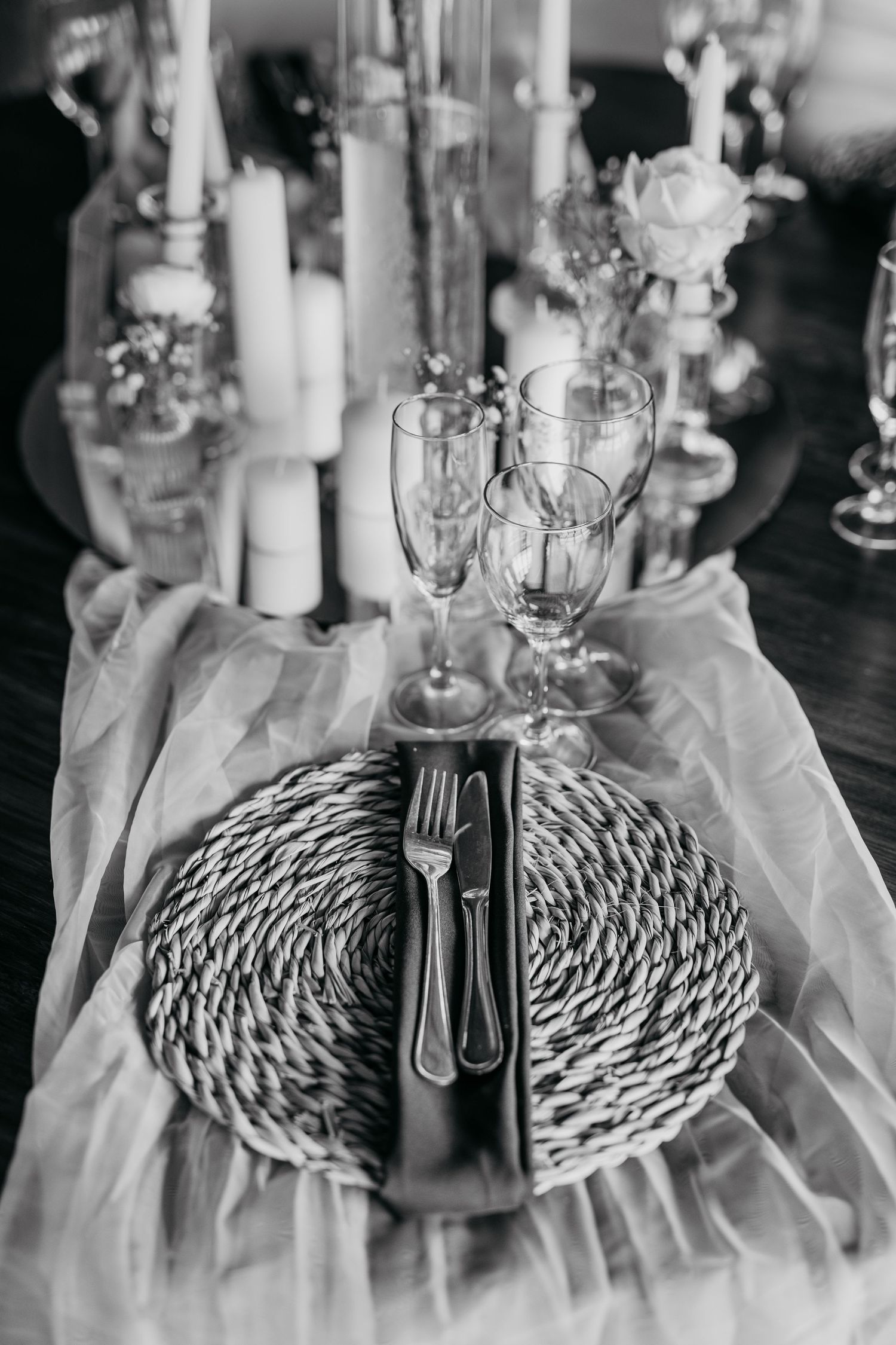 Black and white place setting with a woven charger plate and elegant glassware on a white tablecloth.