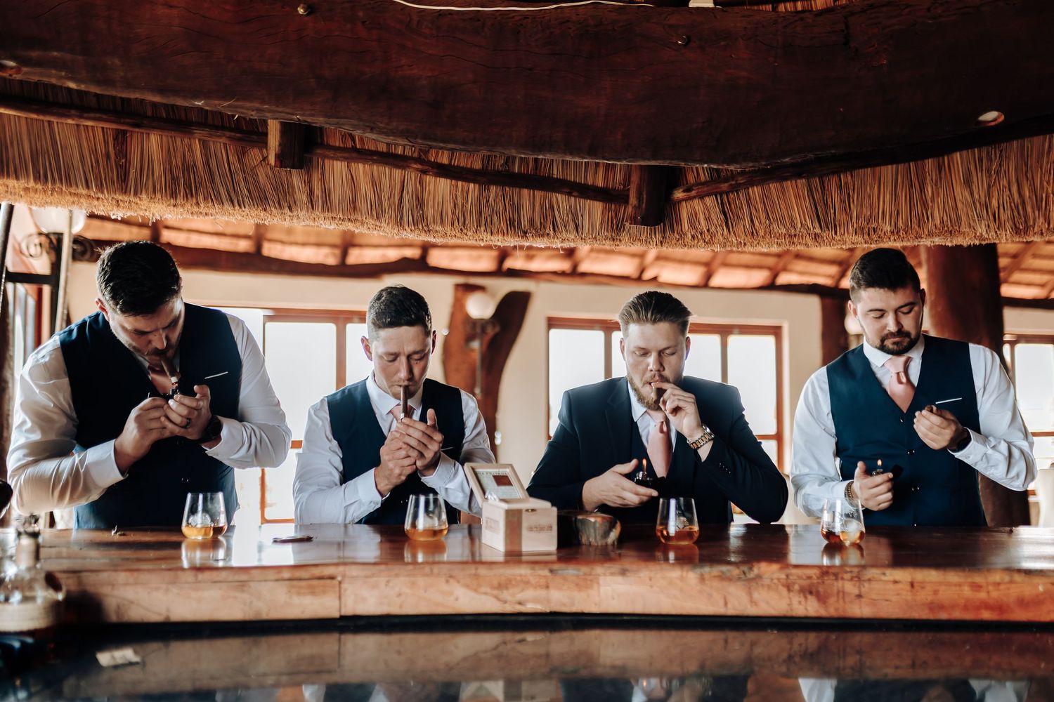 Four men in formalwear sitting at a wooden bar counter all looking down at their phones simultaneously.