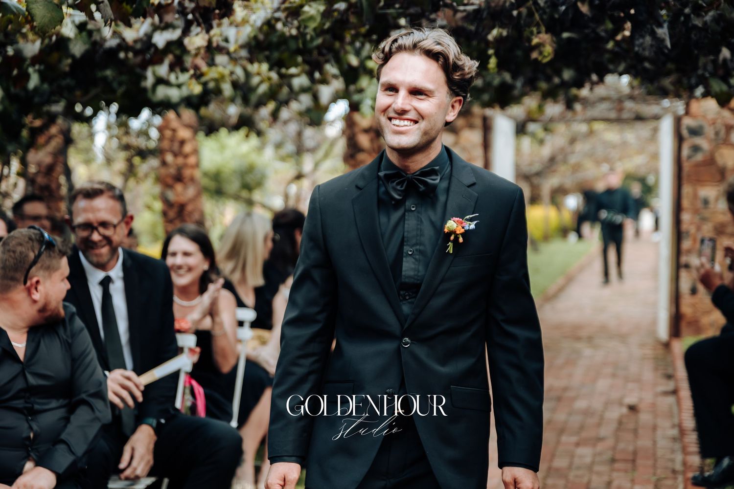 Wedding party walks along brick path surrounded by autumn trees and foliage during outdoor ceremony.