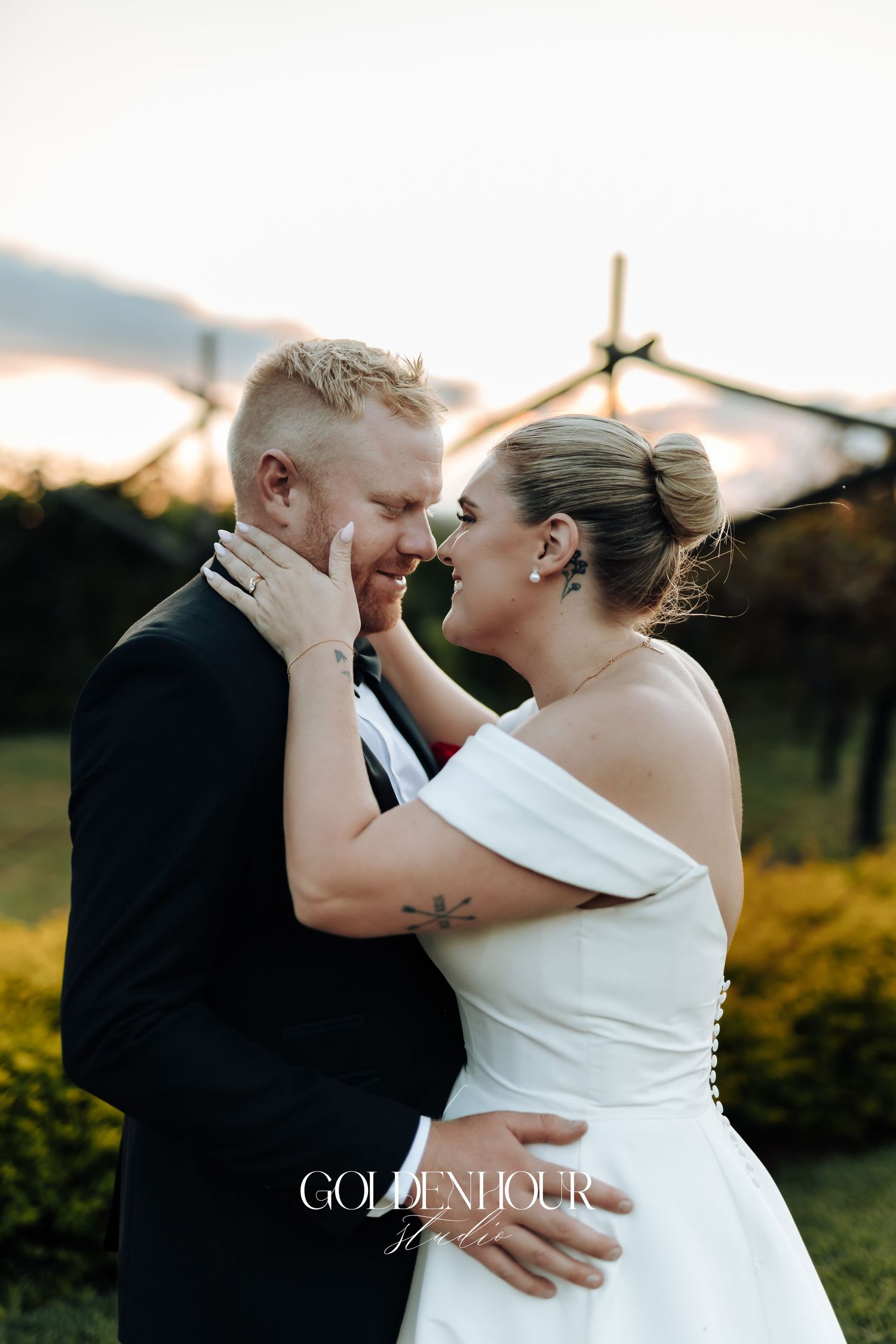 A romantic wedding couple embraces during sunset in a garden setting with golden light illuminating their intimate moment.