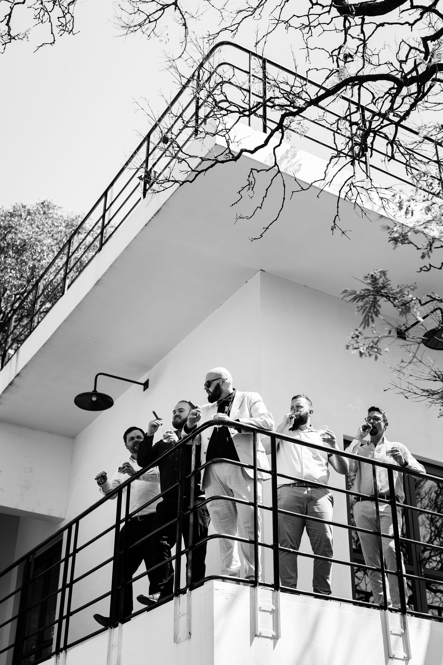 A black and white photograph showing several people standing together on a modern balcony with metal railings.