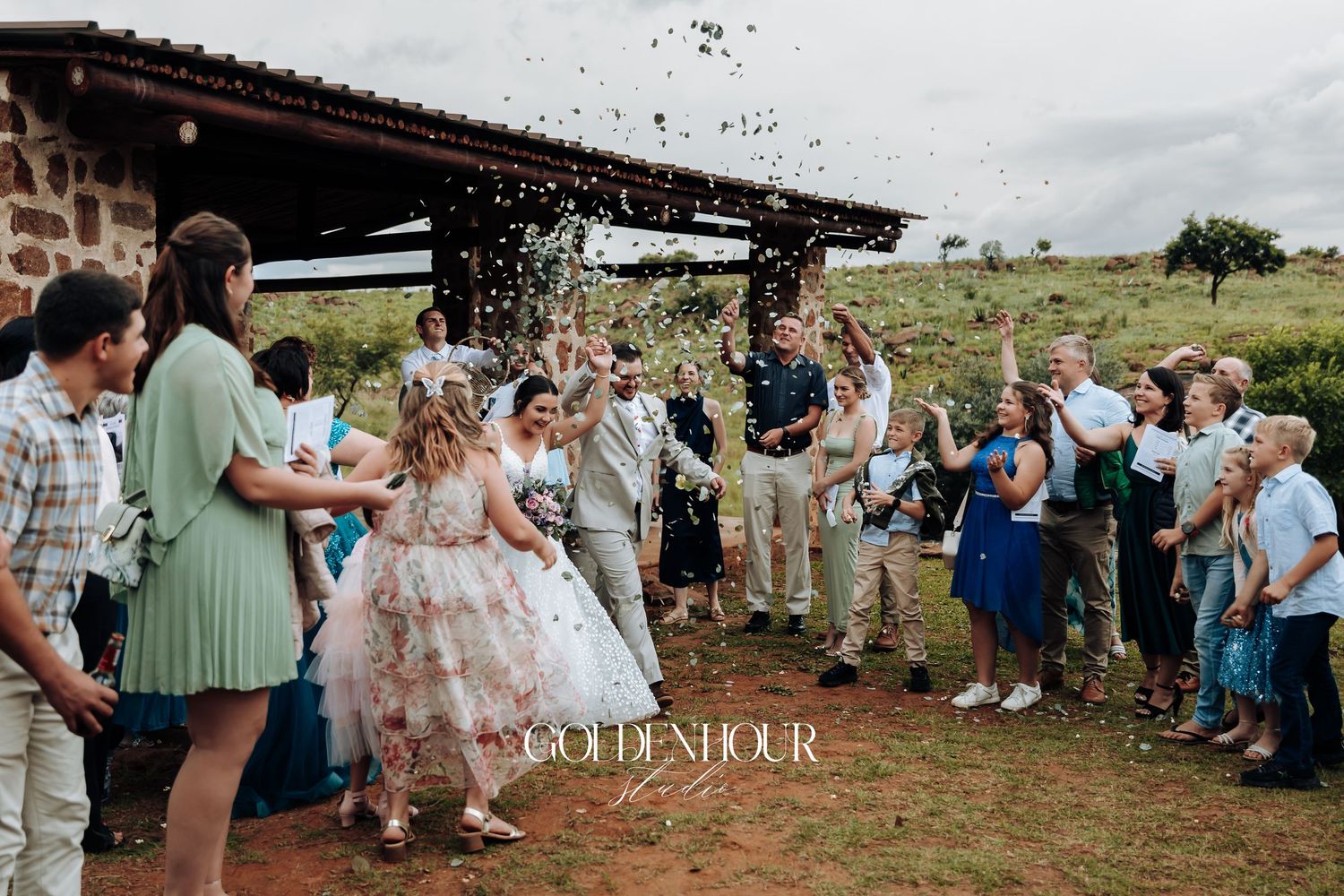 Wedding celebration with guests throwing confetti outside rustic stone building.