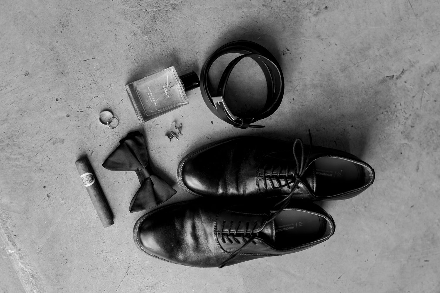 Black and white photo of mens formal dress shoes and accessories laid out on the floor.