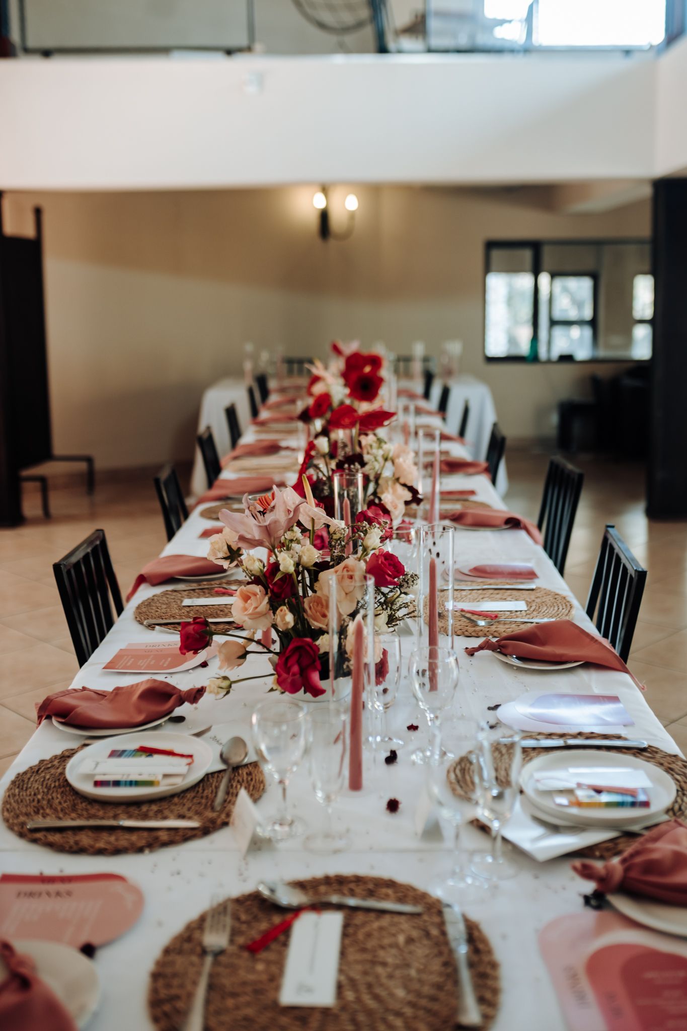 Elegant wedding reception table with red floral centerpieces, woven chargers, and white linens.