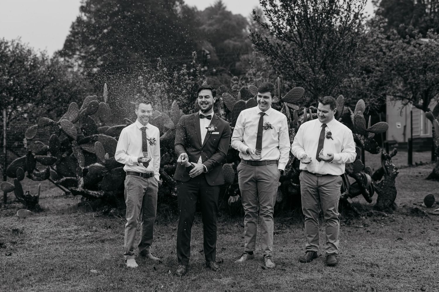 A black and white wedding photo of a wedding party in formal attire standing outdoors.
