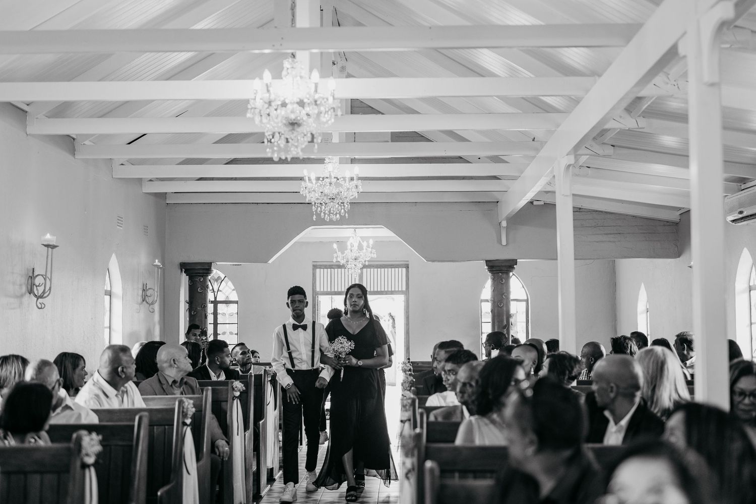 A wedding ceremony at a bright white chapel with exposed wooden beams and crystal chandeliers.