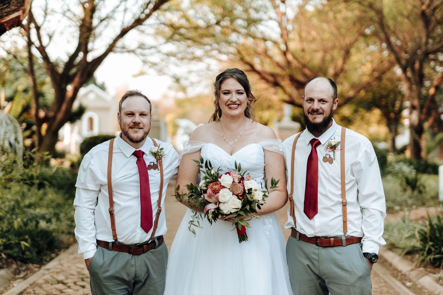 Wedding party members in white shirts and red ties pose with flowers on brick pathway.