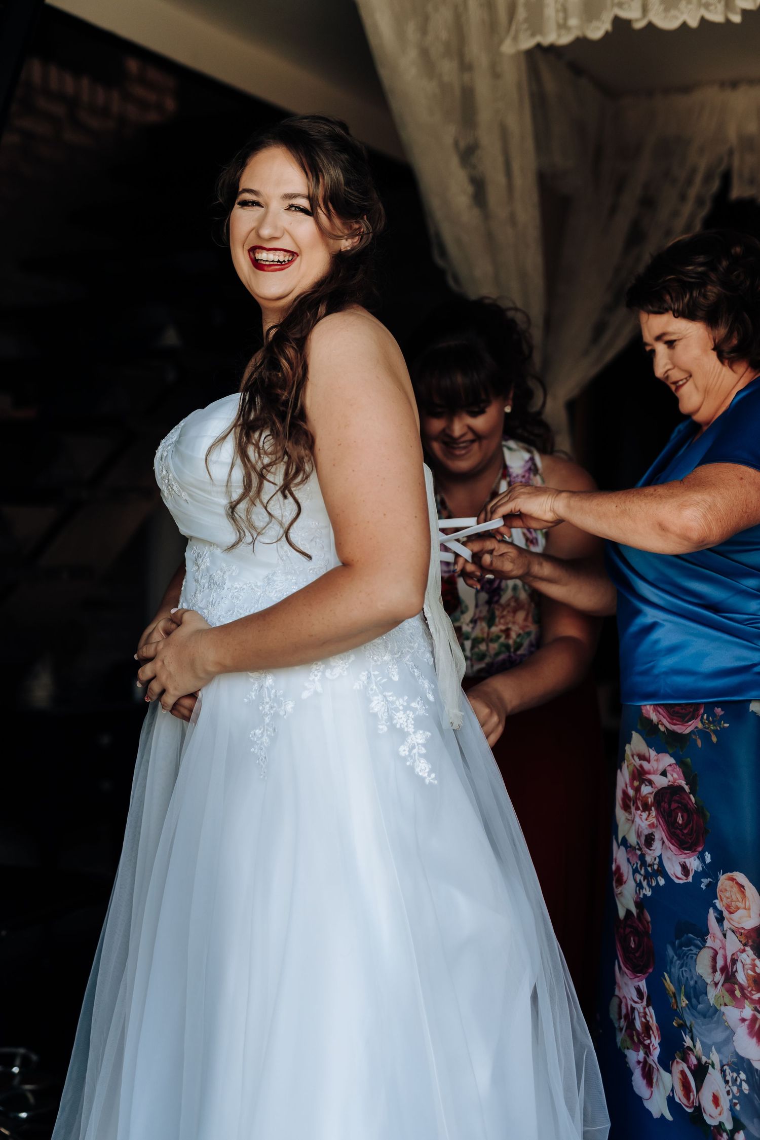 A happy bride wearing an off-shoulder wedding gown smiles radiantly during wedding preparations.