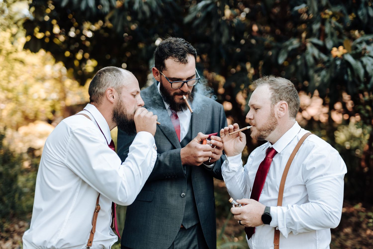 Groomsmen share drinks and laughs during candid outdoor wedding photo moment.